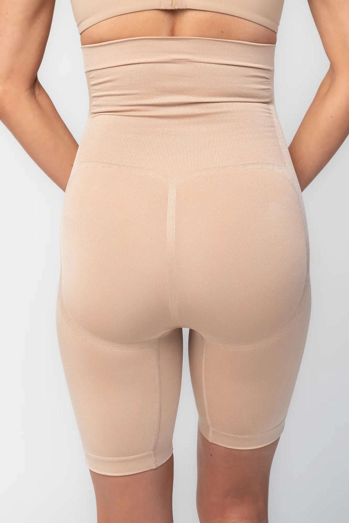 Model wearing nude high-waisted shaping shorts with a seamless design and mid-thigh length.