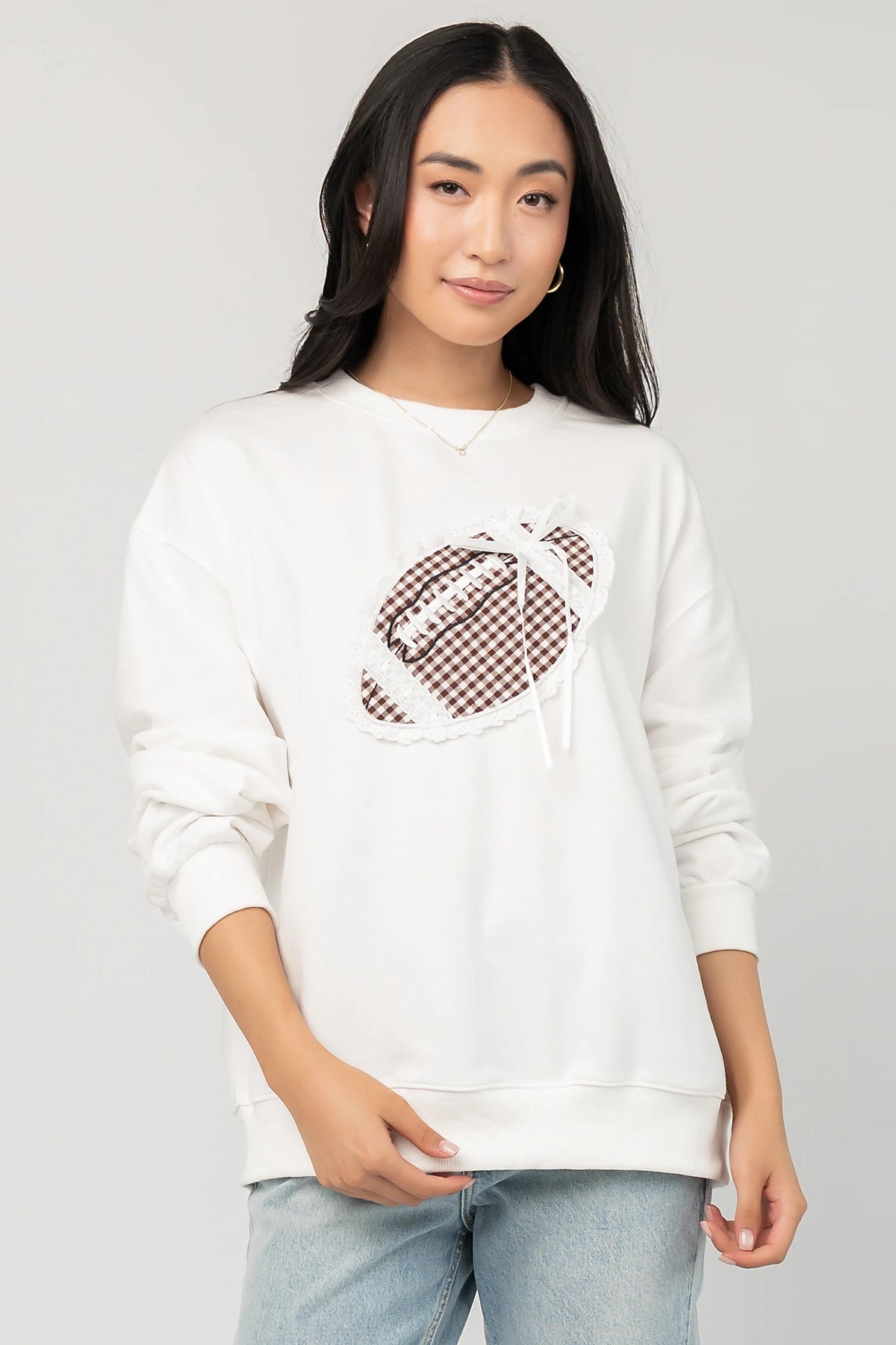 Stephen Gingham Crewneck in Ivory with brown gingham lace appliqué, ribbon bow detail, long sleeves, and ribbed trim.