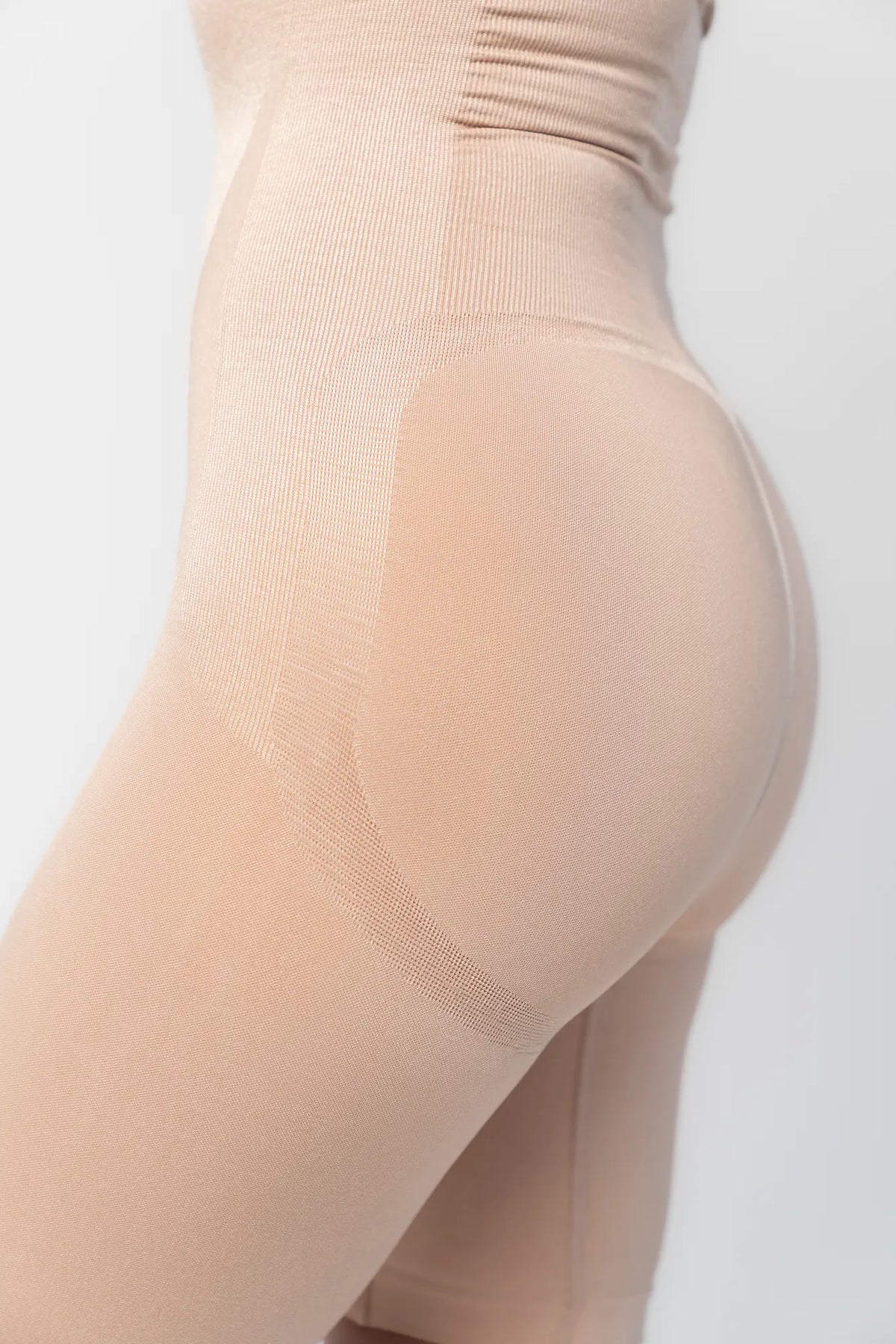 Model wearing nude high-waisted shaping shorts with a seamless design and mid-thigh length.