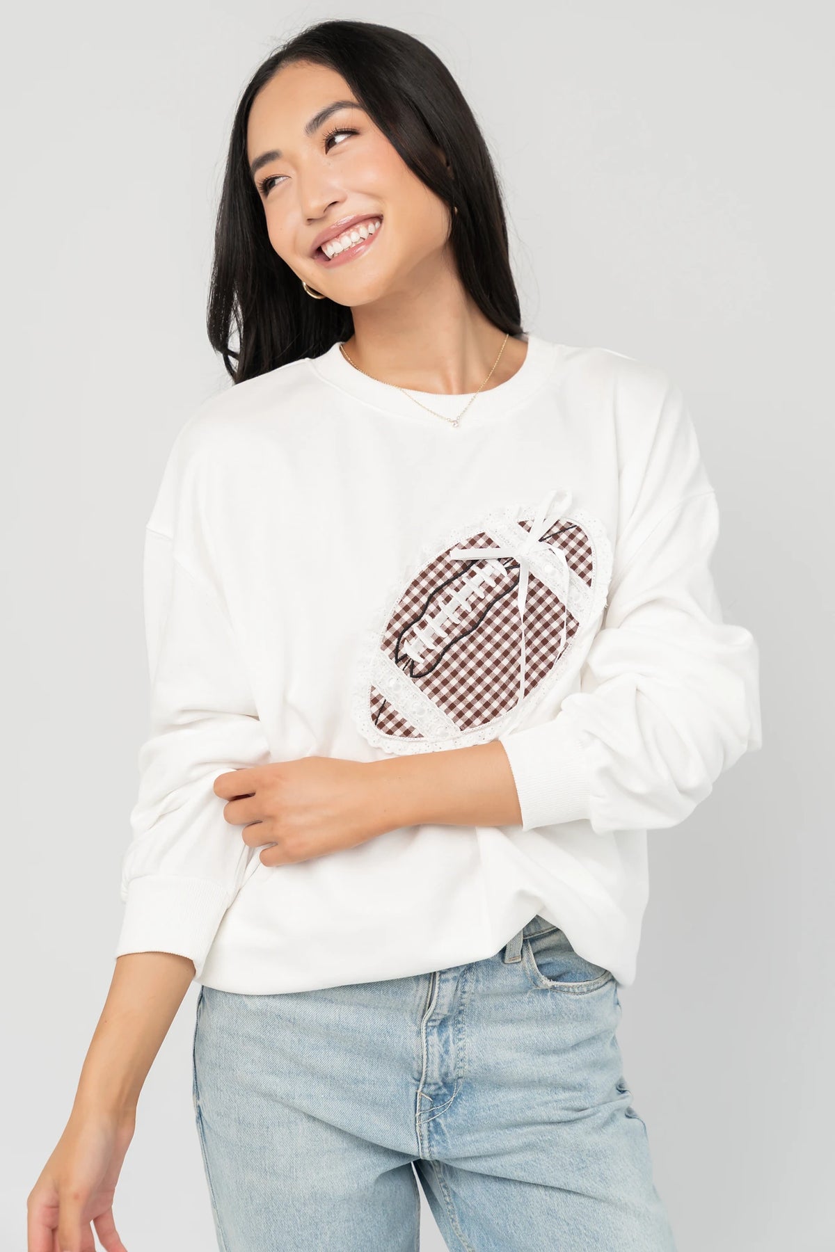 Stephen Gingham Crewneck in Ivory with brown gingham lace appliqué, ribbon bow detail, long sleeves, and ribbed trim.