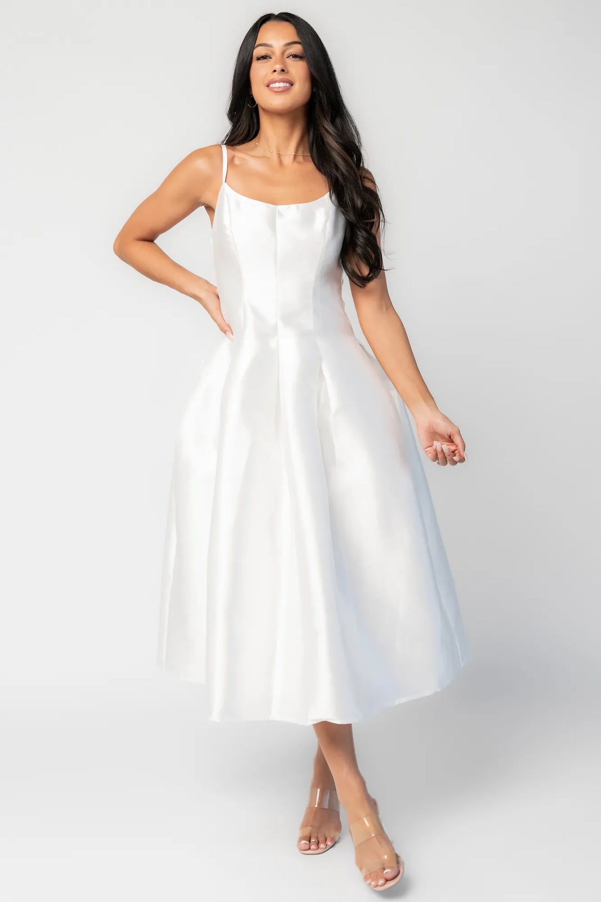 Woman wearing a white sleeveless midi dress with a fitted bodice, side pockets, and a full A-line skirt.