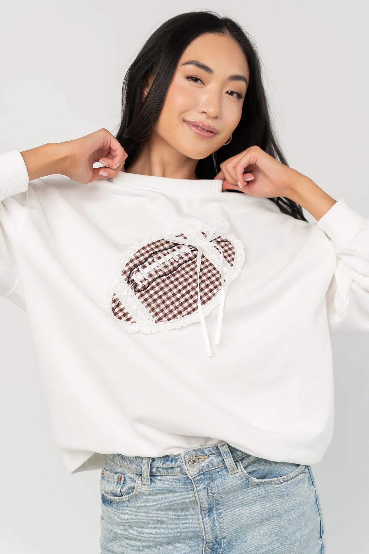 Stephen Gingham Crewneck in Ivory with brown gingham lace appliqué, ribbon bow detail, long sleeves, and ribbed trim.