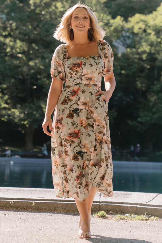 Model wearing the Charlotte Midi Dress in Sage, a sage green midi dress with a pink multi floral print, rounded square neckline, puff sleeves, banded waist, and flowing A-line skirt with side pockets.