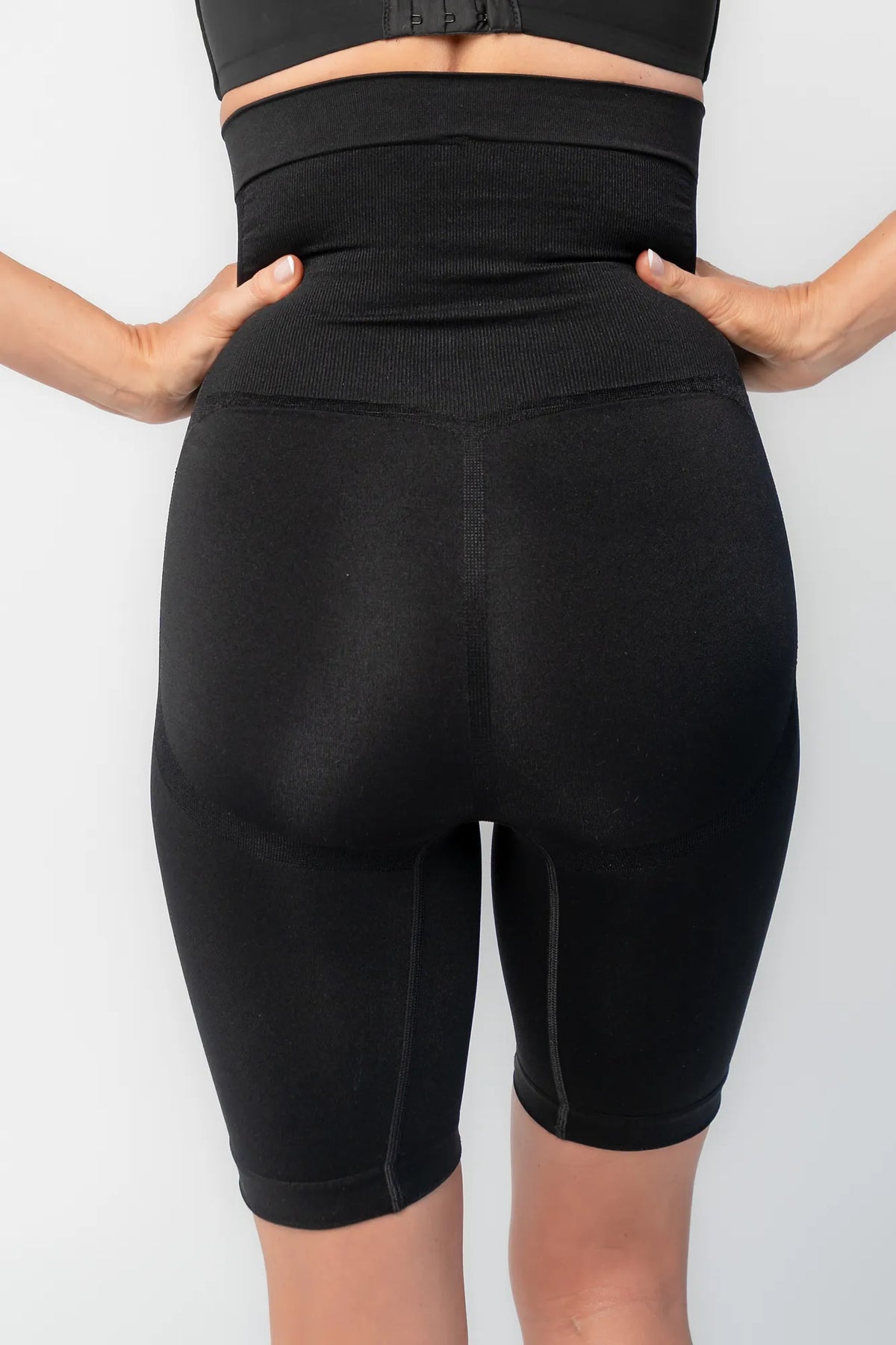 Model wearing black high-waisted shaping shorts with a seamless design and mid-thigh length.