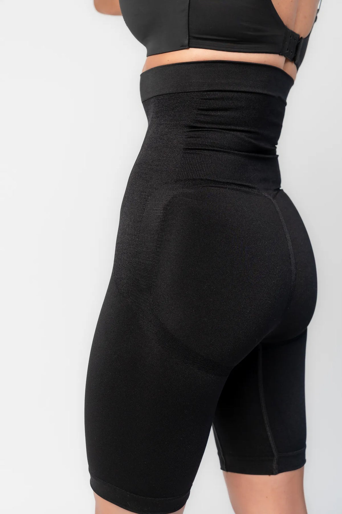 Model wearing black high-waisted shaping shorts with a seamless design and mid-thigh length.