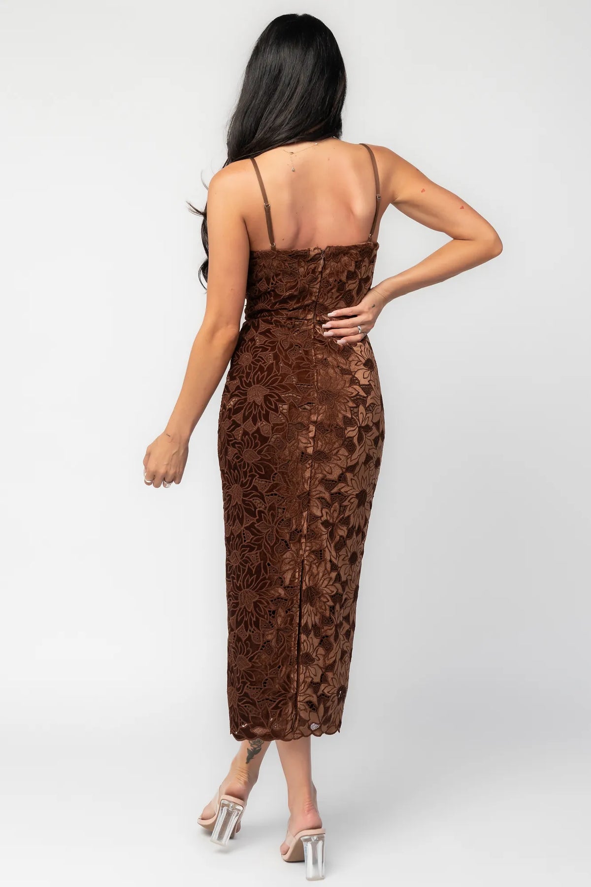 Model wearing a fitted espresso brown midi dress featuring an allover floral velvet lace overlay. The dress has a square neckline, adjustable spaghetti straps, and a body-skimming silhouette that falls below the knee with a scalloped hem.