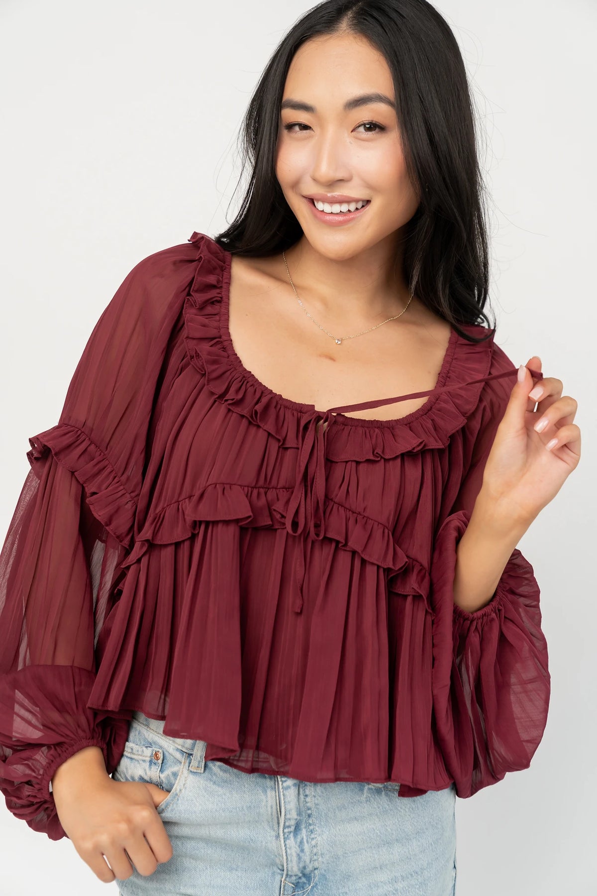Bellerose Ruffle Top in Burgundy with pleated chiffon, ruffle-trimmed neckline, front tie, and billowy long sleeves.