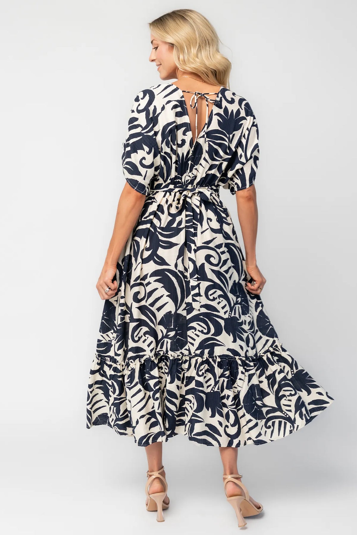 Woman wearing a navy and ivory printed midi dress with a V-neckline, short sleeves, an empire waist, and a tiered hem.