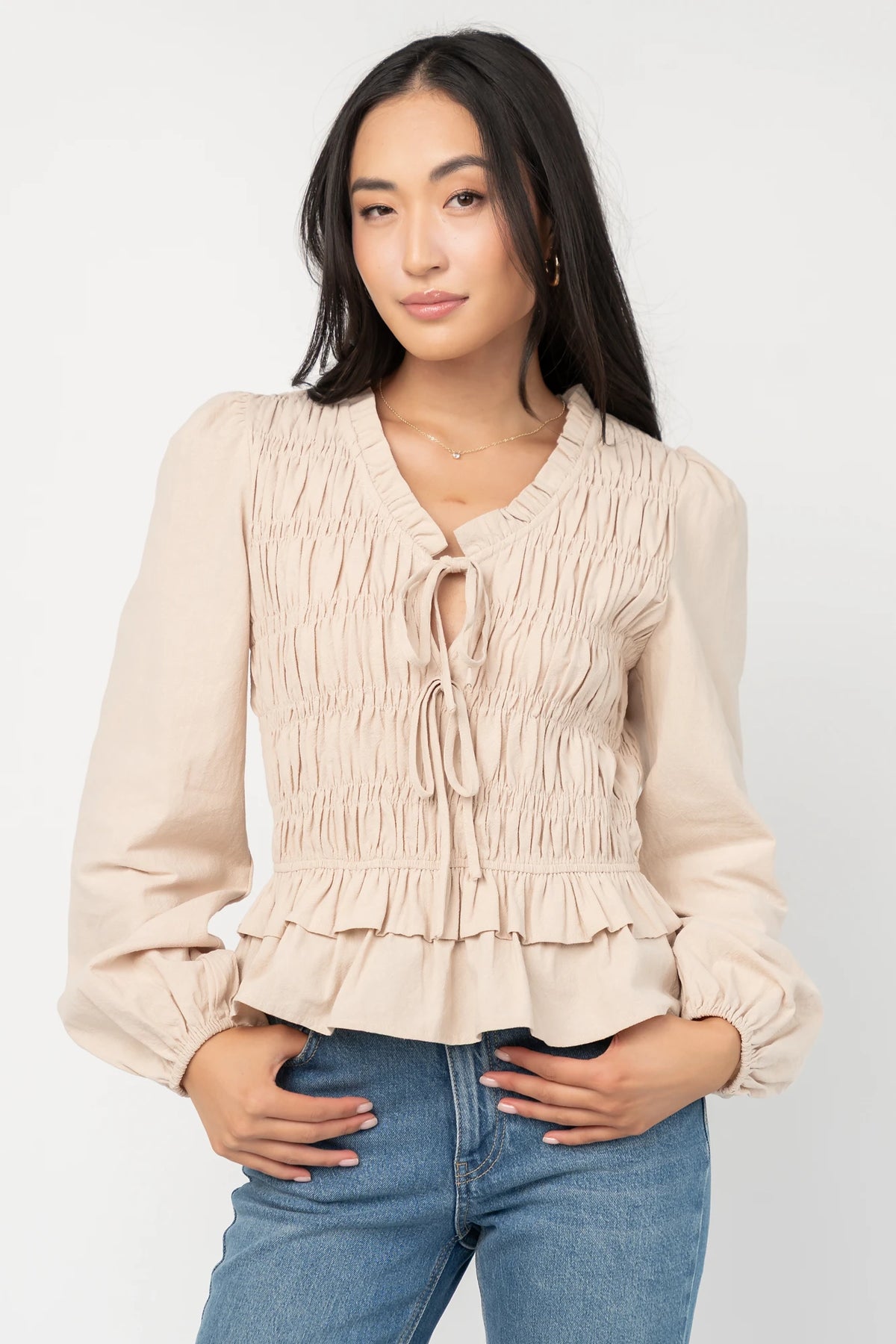 Marnie Smocked Top in Natural with smocked bodice, front bow ties, long sleeves, elastic cuffs, and peplum hem.