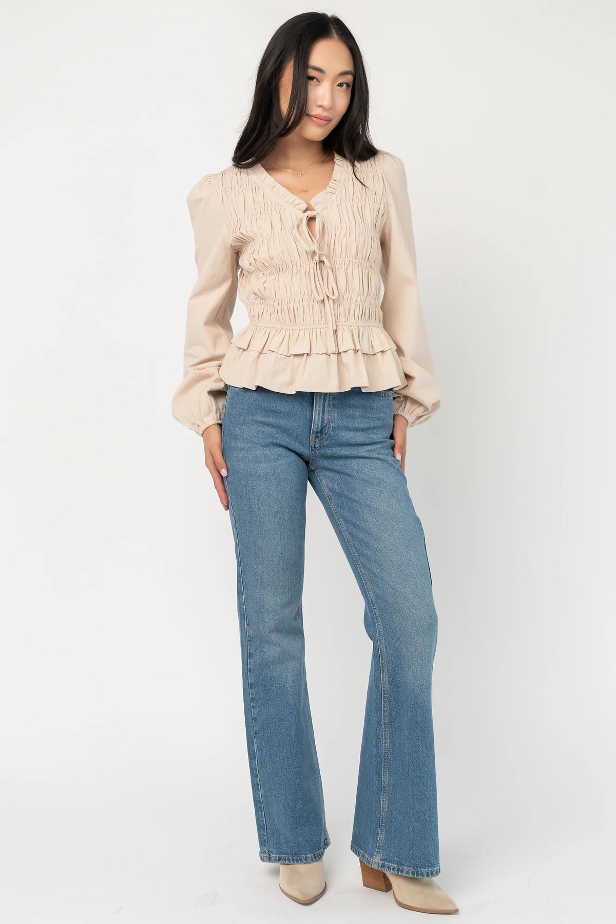 Marnie Smocked Top in Natural with smocked bodice, front bow ties, long sleeves, elastic cuffs, and peplum hem.