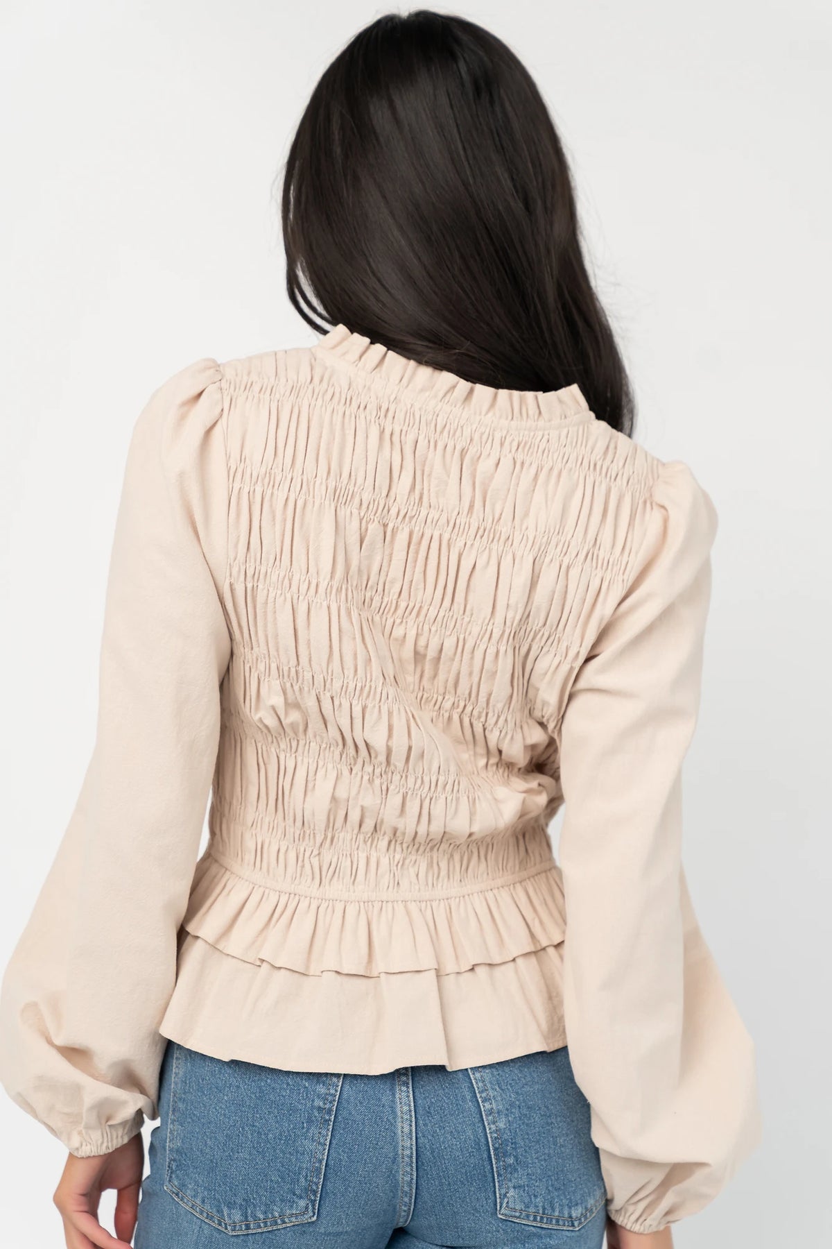 Marnie Smocked Top in Natural with smocked bodice, front bow ties, long sleeves, elastic cuffs, and peplum hem.