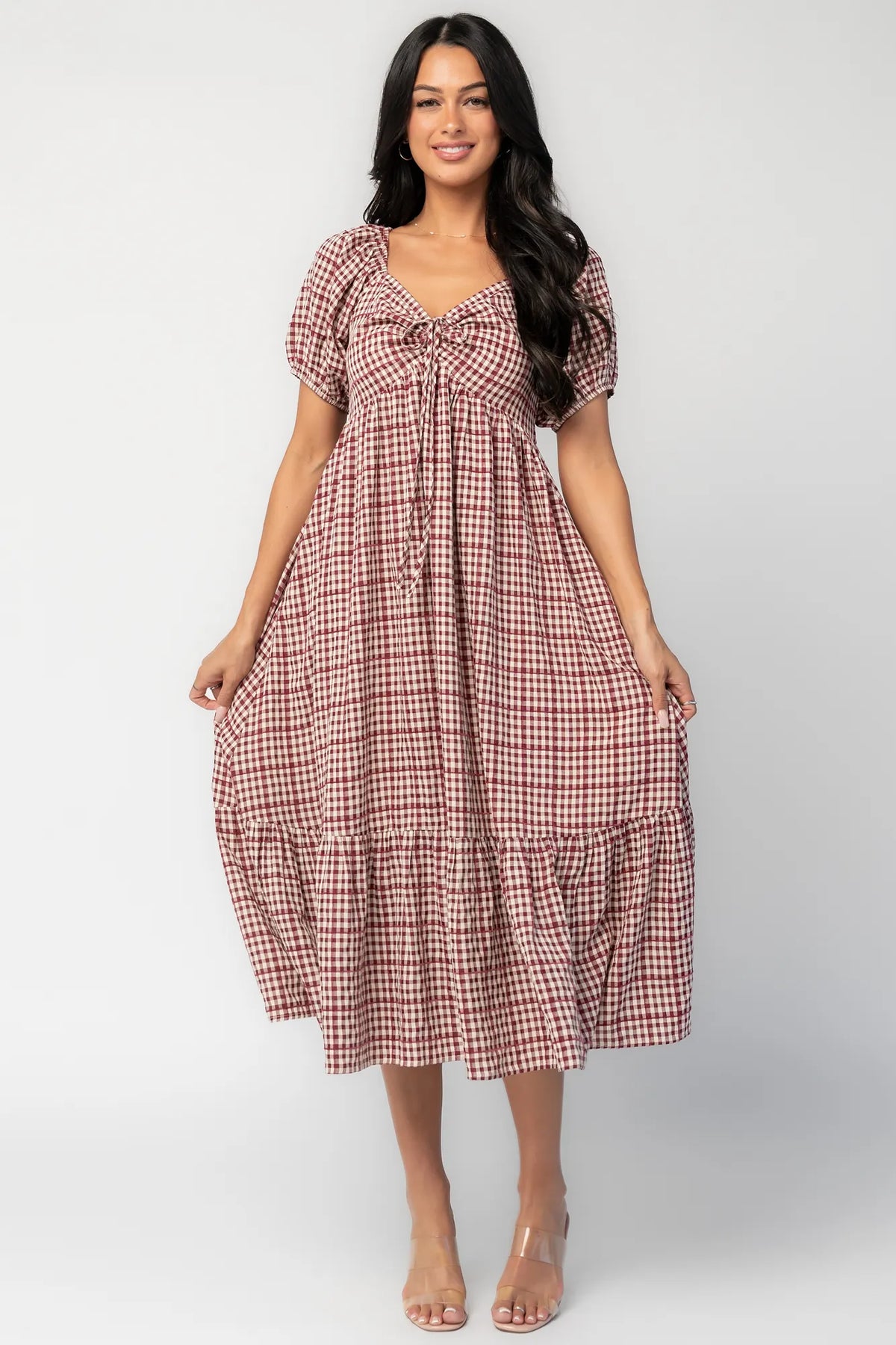 Model wearing a berry and cream plaid midi dress with a sweetheart neckline, front tie detail, and oversized puff sleeves.