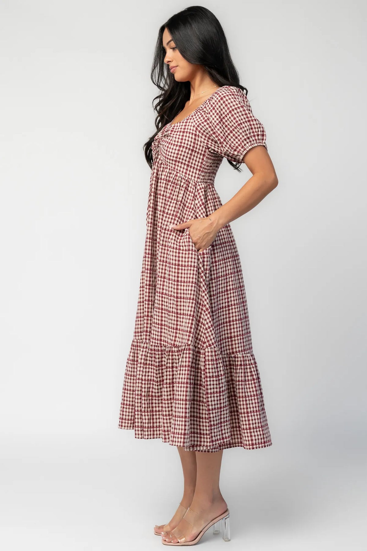 Model wearing a berry and cream plaid midi dress with a sweetheart neckline, front tie detail, and oversized puff sleeves.