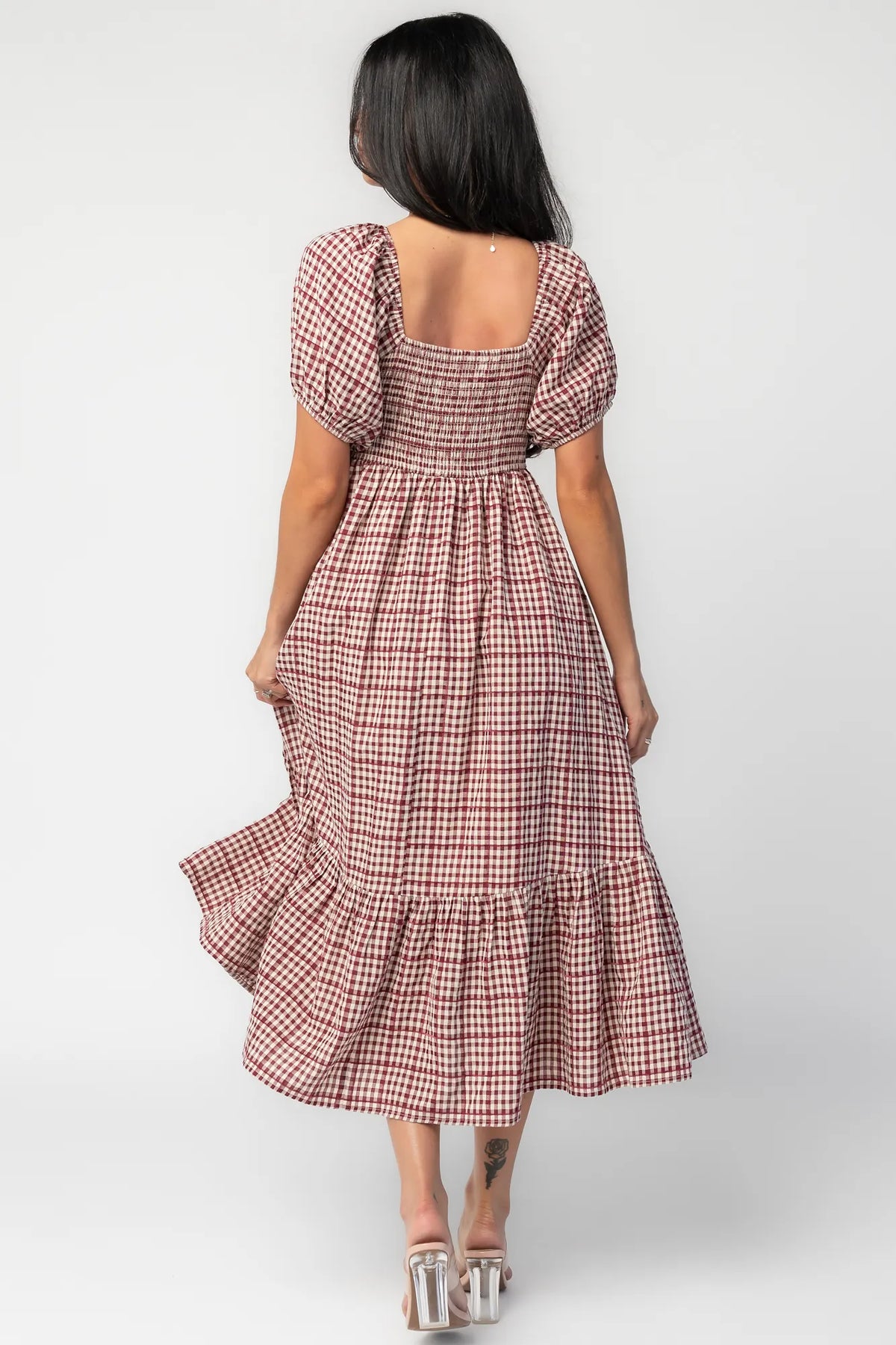 Model wearing a berry and cream plaid midi dress with a sweetheart neckline, front tie detail, and oversized puff sleeves.