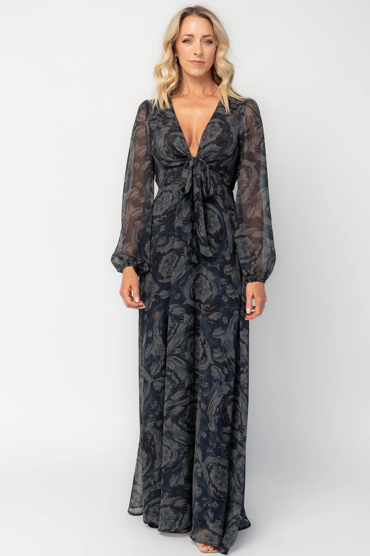 Model wearing a midnight blue floral maxi dress with a deep V-neckline and front tie keyhole detail.