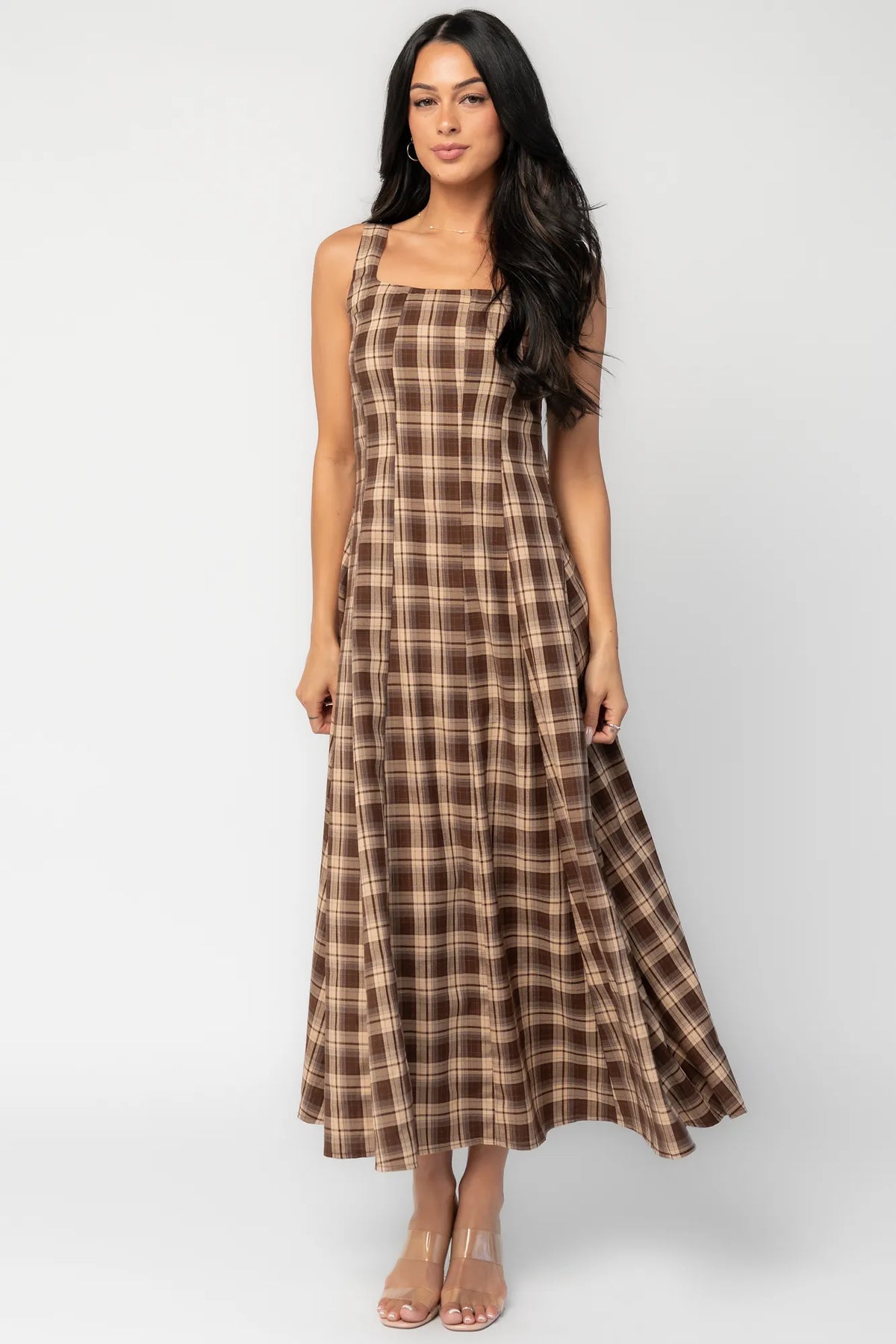 Model wearing a brown and taupe plaid maxi dress with a square neckline and wide tank straps. The dress features a fitted bodice with princess seam detailing, a defined waist, and a flowing full-length skirt.