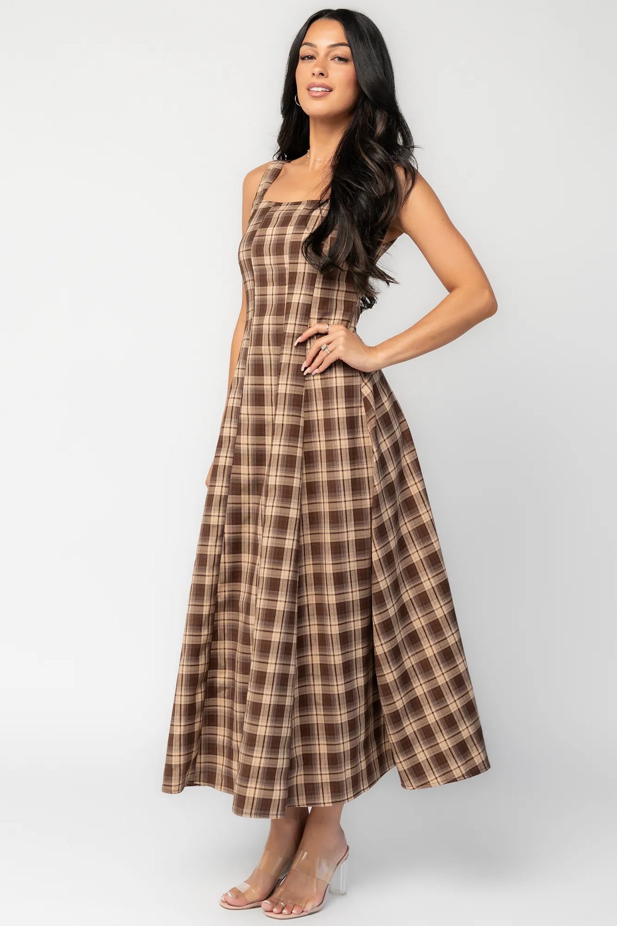 Model wearing a brown and taupe plaid maxi dress with a square neckline and wide tank straps. The dress features a fitted bodice with princess seam detailing, a defined waist, and a flowing full-length skirt.