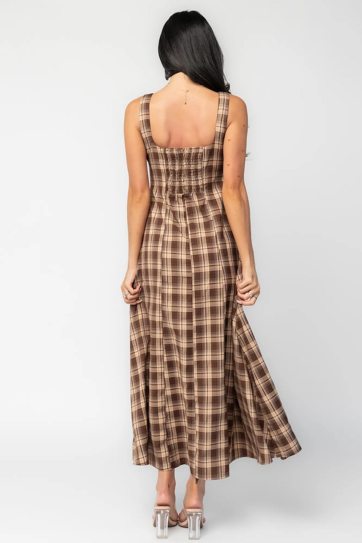 Model wearing a brown and taupe plaid maxi dress with a square neckline and wide tank straps. The dress features a fitted bodice with princess seam detailing, a defined waist, and a flowing full-length skirt.