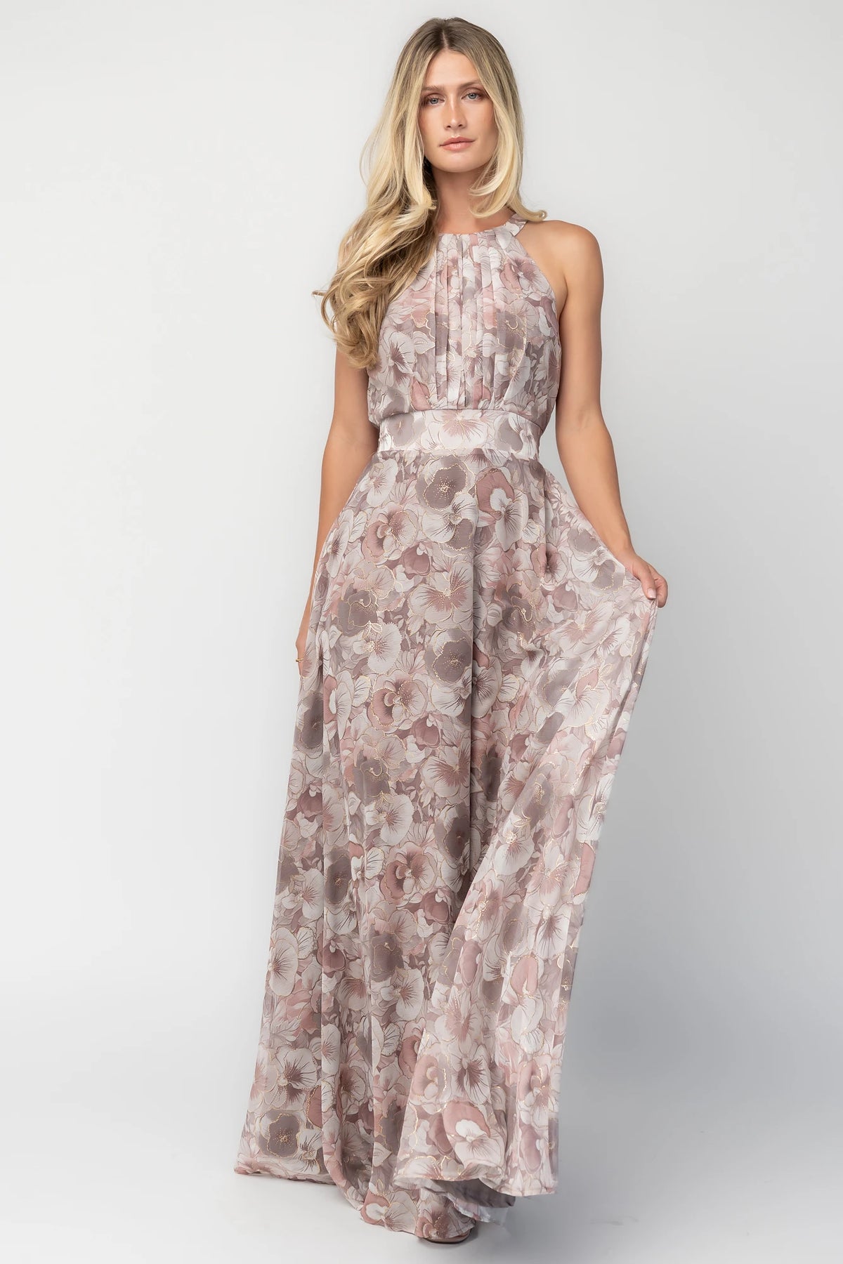 Model wearing the Tinsley Metallic Maxi Dress in Dusty Mauve featuring a high pleated halter neckline, defined waistband, tie-back keyhole detail, and a flowing chiffon maxi skirt with a dusty mauve floral print and subtle metallic shimmer.