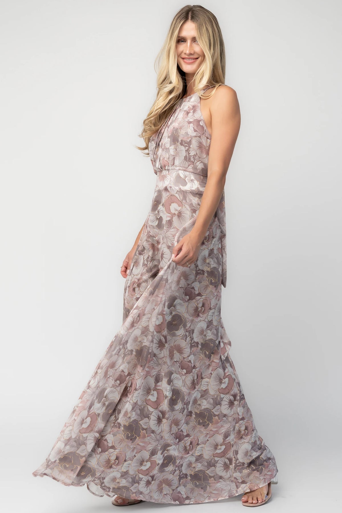 Model wearing the Tinsley Metallic Maxi Dress in Dusty Mauve featuring a high pleated halter neckline, defined waistband, tie-back keyhole detail, and a flowing chiffon maxi skirt with a dusty mauve floral print and subtle metallic shimmer.