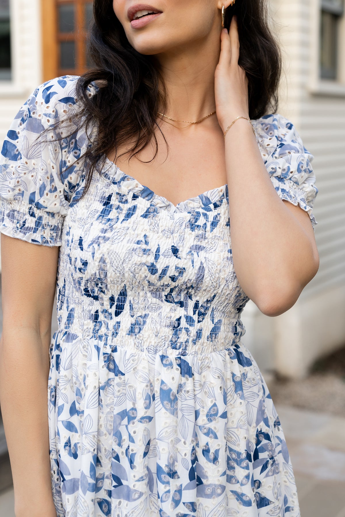 Styled lifestyle image of off-white and blue floral eyelet midi dress paired with neutral sandals for a daytime occasion.