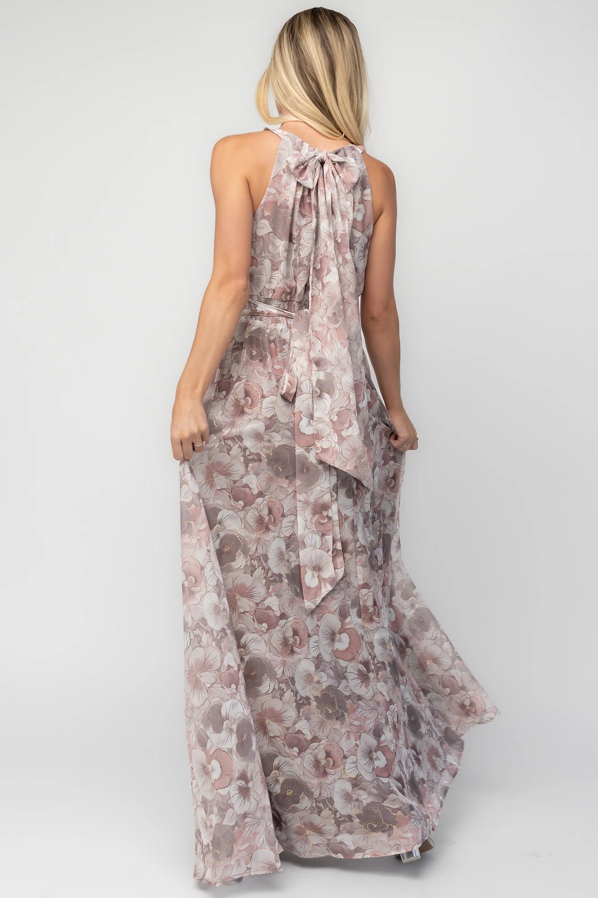 Model wearing the Tinsley Metallic Maxi Dress in Dusty Mauve featuring a high pleated halter neckline, defined waistband, tie-back keyhole detail, and a flowing chiffon maxi skirt with a dusty mauve floral print and subtle metallic shimmer.