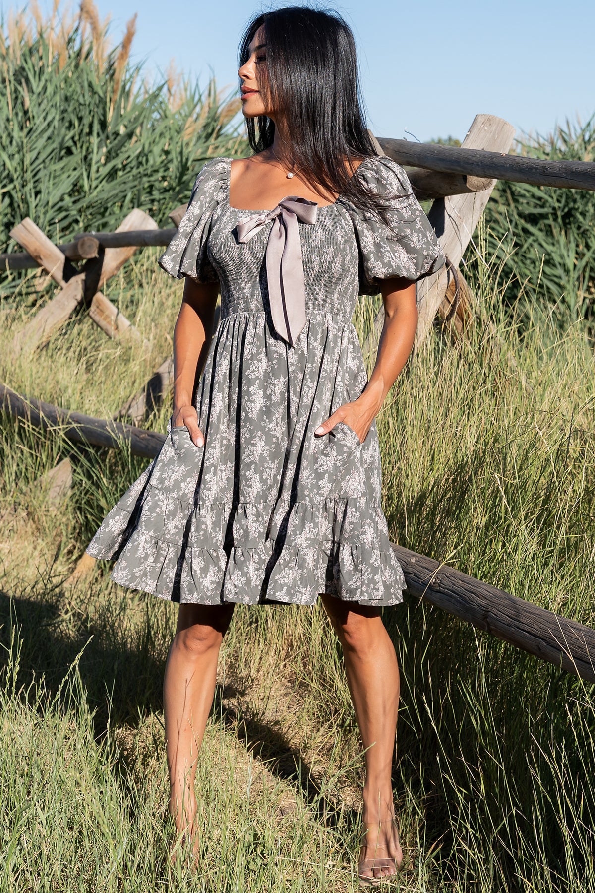 Back and side composition of the Anastasia Bow Short Dress on model, showing tiered skirt layers, back fit, and the printed dusty olive floral pattern.