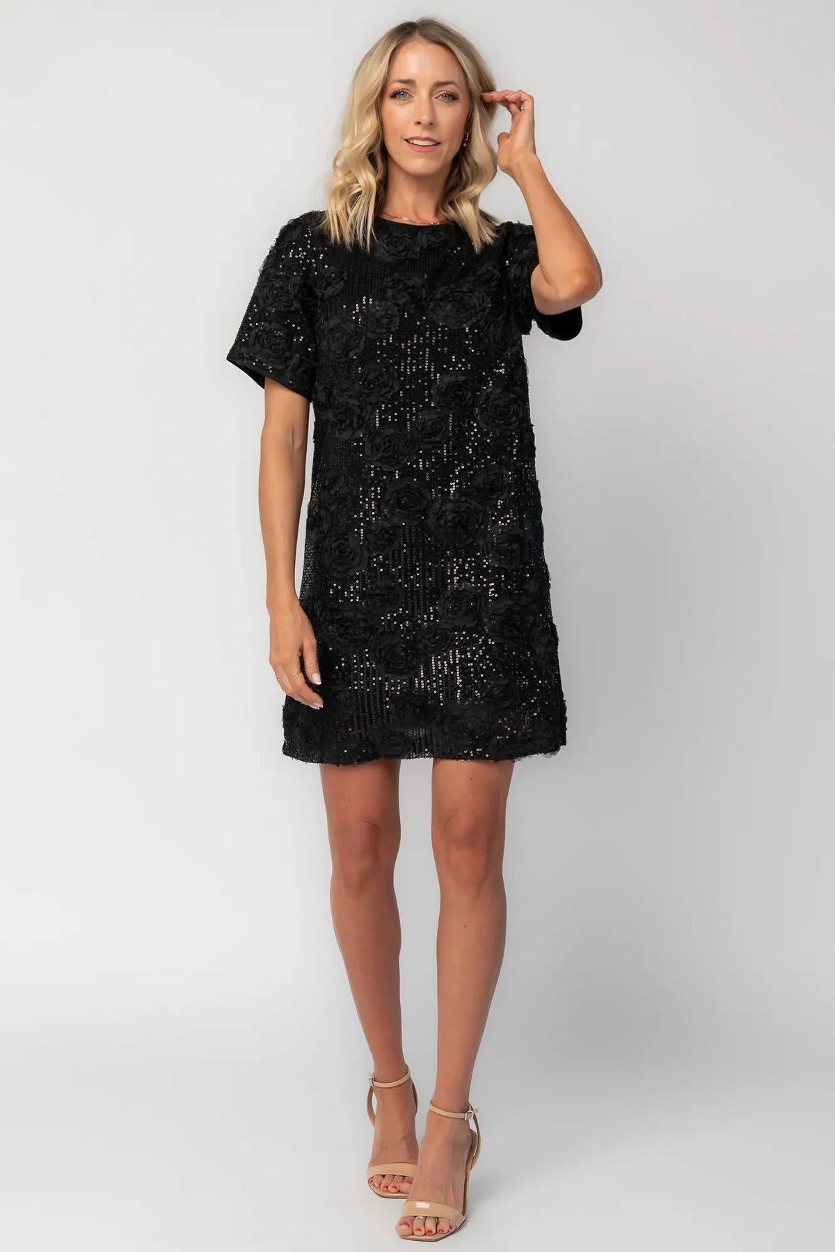 Model wearing a black short shift dress embellished with green sequins and floral appliqué detailing.