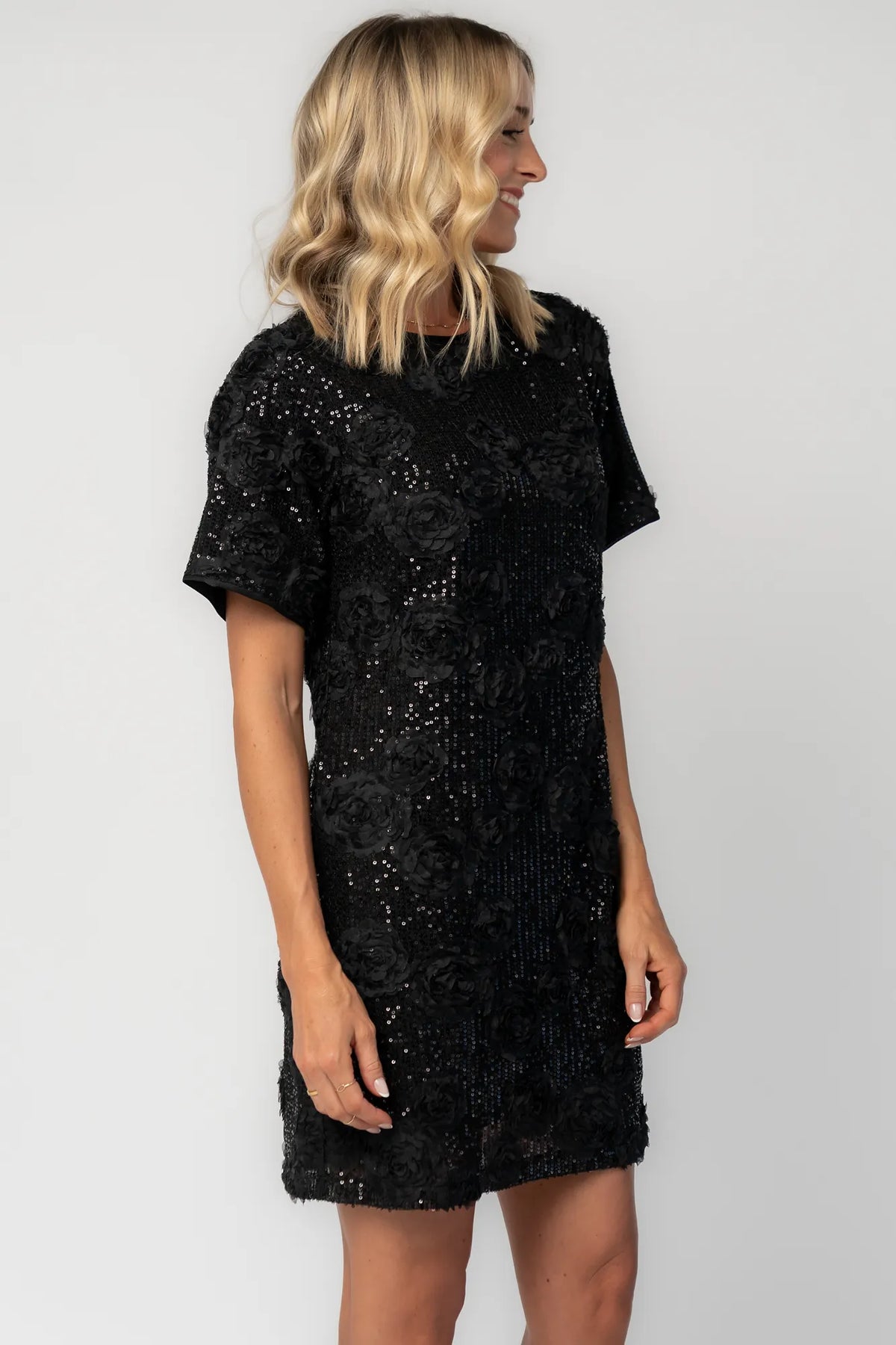 Model wearing a black short shift dress embellished with green sequins and floral appliqué detailing.