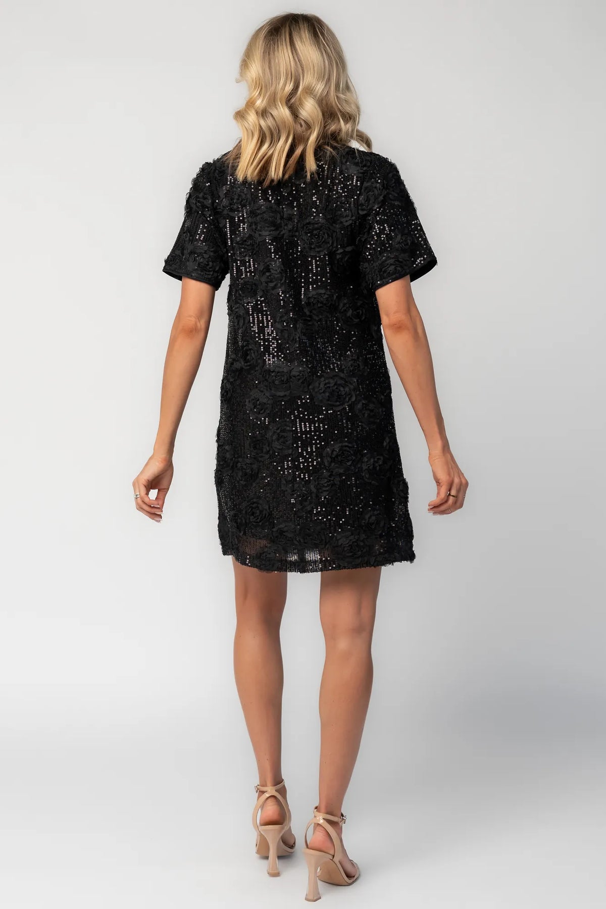 Model wearing a black short shift dress embellished with green sequins and floral appliqué detailing.