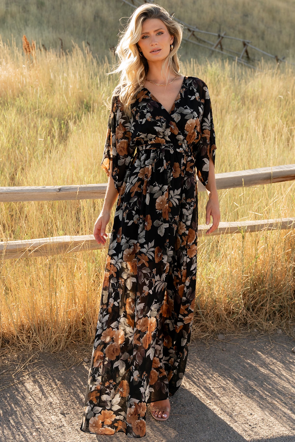 Front view of model wearing the Kia Kimono Maxi Dress in black with copper and light gray floral pattern, full-length and draped.