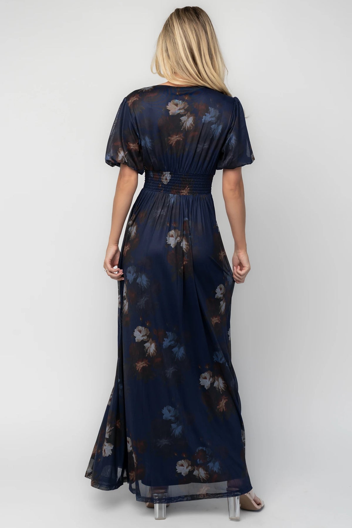 Model wearing the Whitney Mesh Maxi Dress in Navy, a navy floral mesh maxi dress with a deep V-neckline, short flutter sleeves, an empire waist, and a flowing A-line skirt with side pockets.