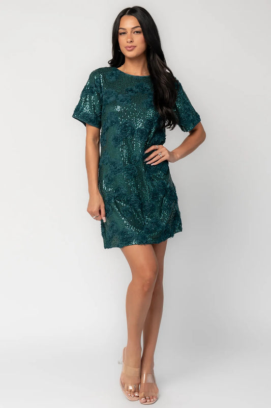Model wearing a green short shift dress embellished with green sequins and floral appliqué detailing.