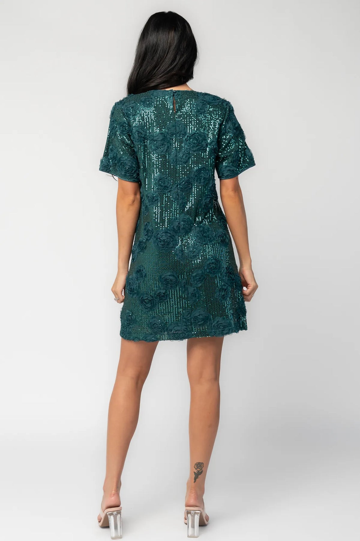 Model wearing a green short shift dress embellished with green sequins and floral appliqué detailing.