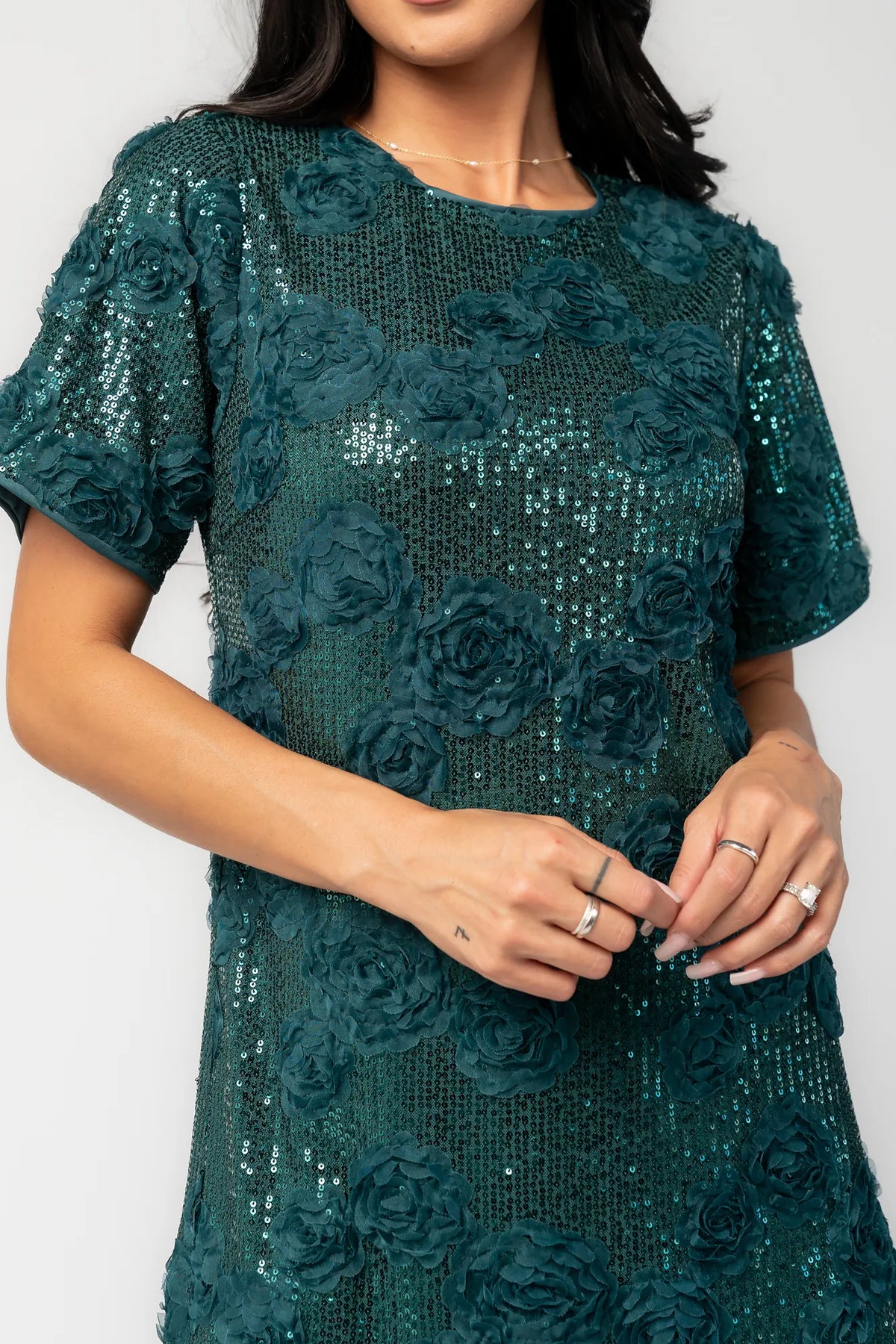 Model wearing a green short shift dress embellished with green sequins and floral appliqué detailing.