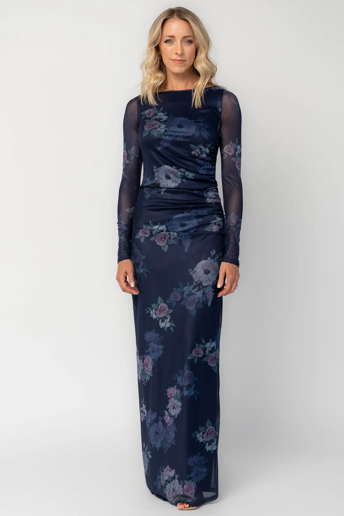 Model wearing a deep plum floral maxi dress with a fitted bodycon silhouette, sheer long sleeves, and a round neckline.