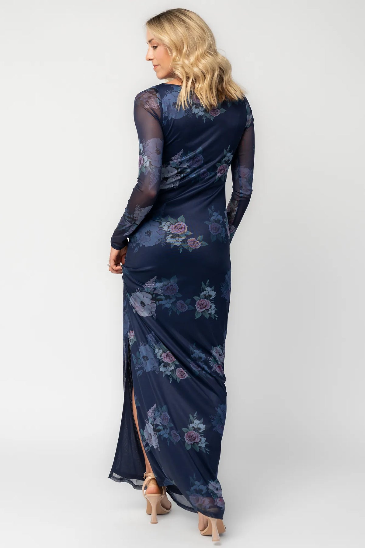 Model wearing a deep plum floral maxi dress with a fitted bodycon silhouette, sheer long sleeves, and a round neckline.