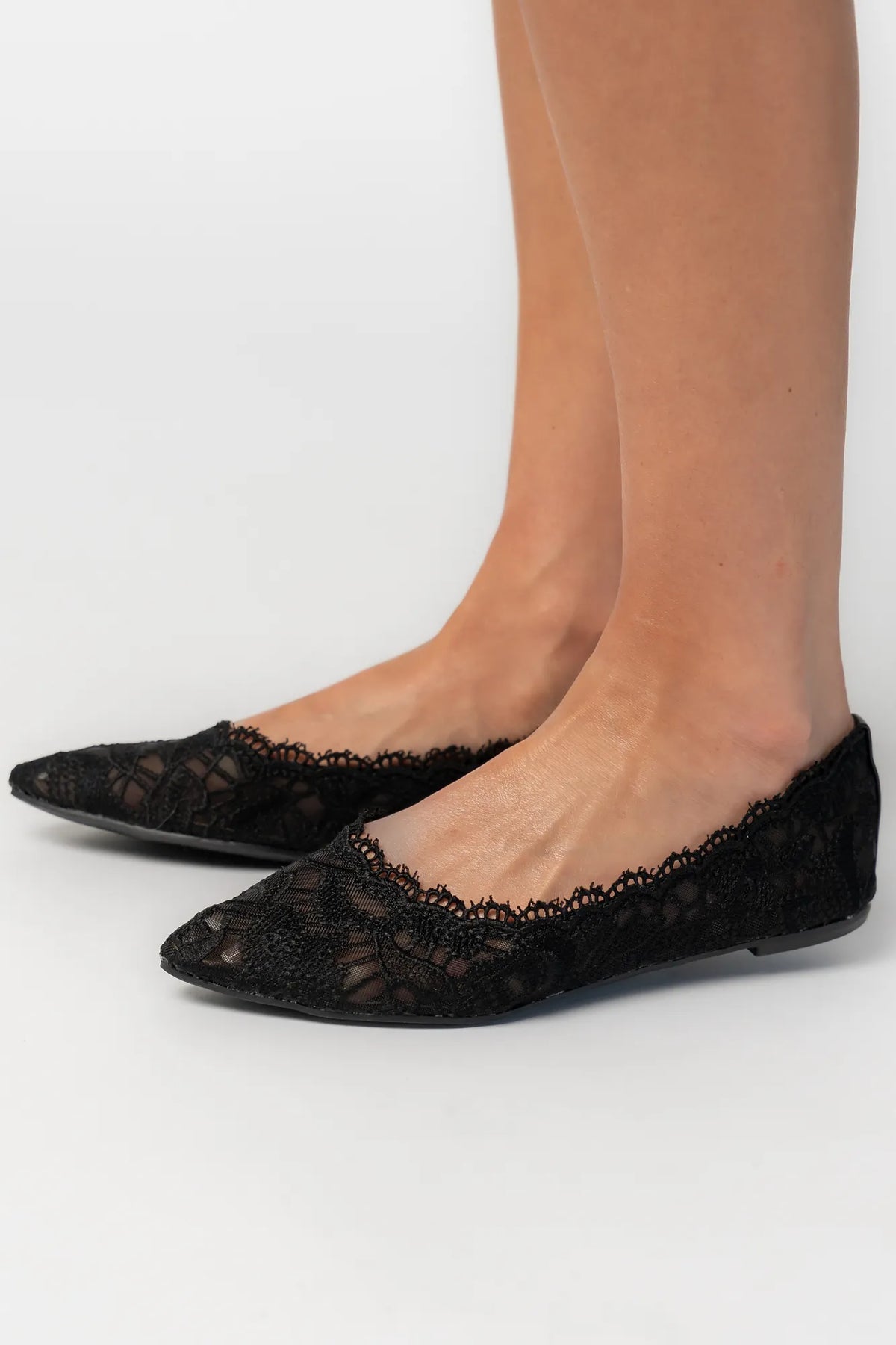 Model wearing black lace ballet flats with a pointed toe, sheer lace construction, and scalloped edges. The feminine flat silhouette offers an elegant, lightweight look.