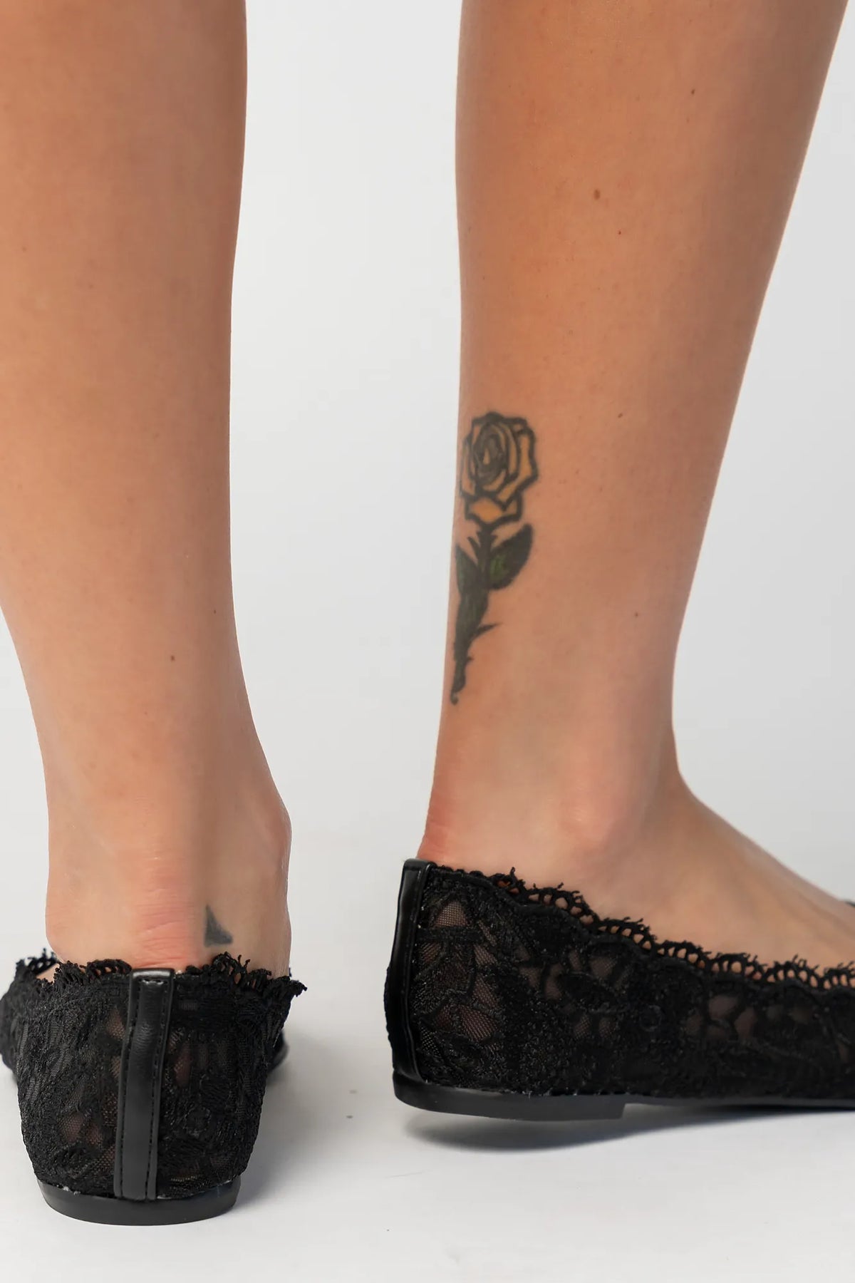 Model wearing black lace ballet flats with a pointed toe, sheer lace construction, and scalloped edges. The feminine flat silhouette offers an elegant, lightweight look.