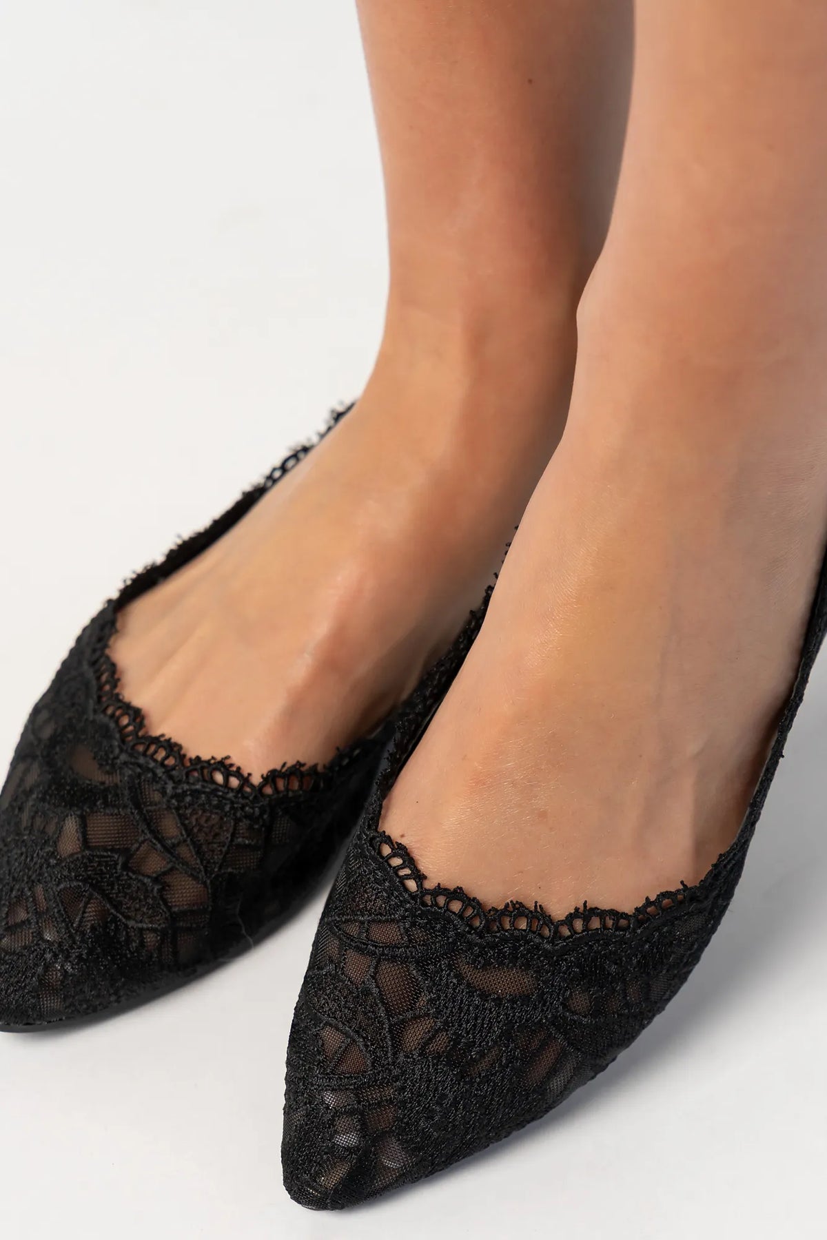 Model wearing black lace ballet flats with a pointed toe, sheer lace construction, and scalloped edges. The feminine flat silhouette offers an elegant, lightweight look.