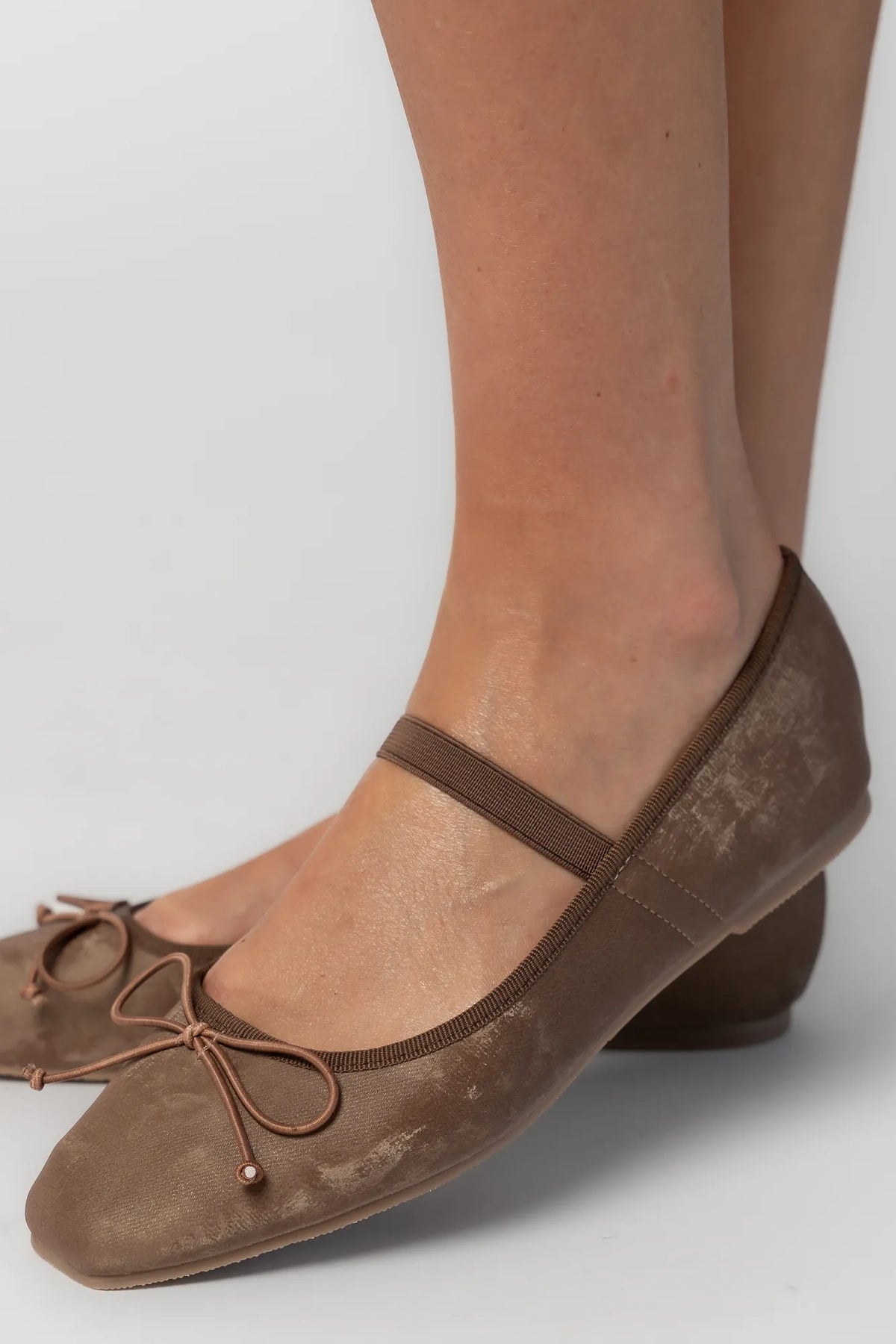 Pair of mocha velvet Mary Jane ballet flats featuring a square toe, delicate bow detail, and elastic strap across the foot. The classic flat silhouette offers a timeless, feminine look for everyday wear.