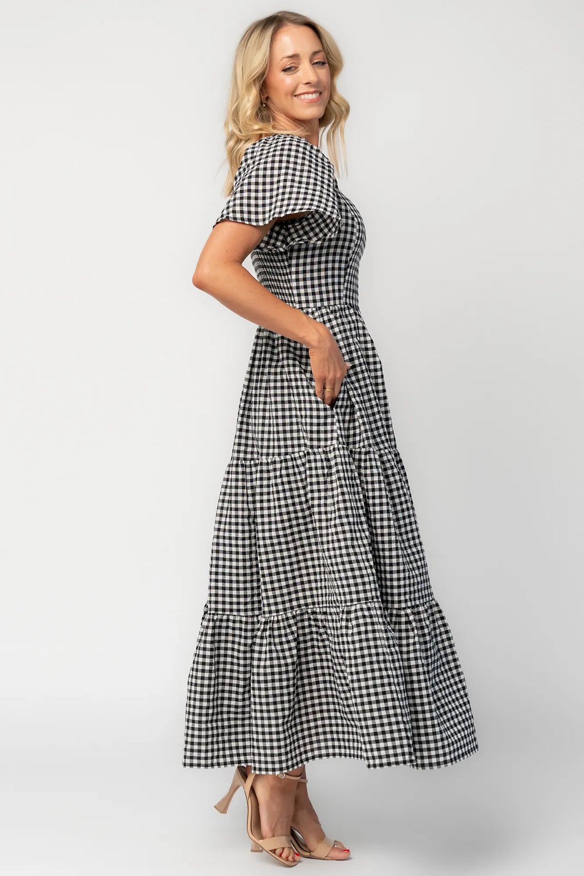 Model wearing a black and white gingham maxi dress with a square neckline, flutter sleeves, and a fitted bodice.