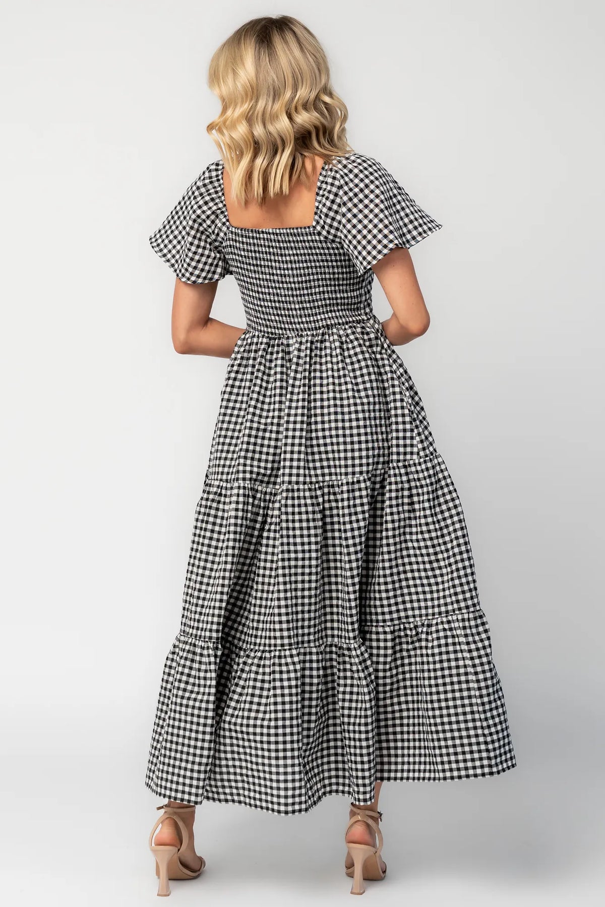 Model wearing a black and white gingham maxi dress with a square neckline, flutter sleeves, and a fitted bodice.
