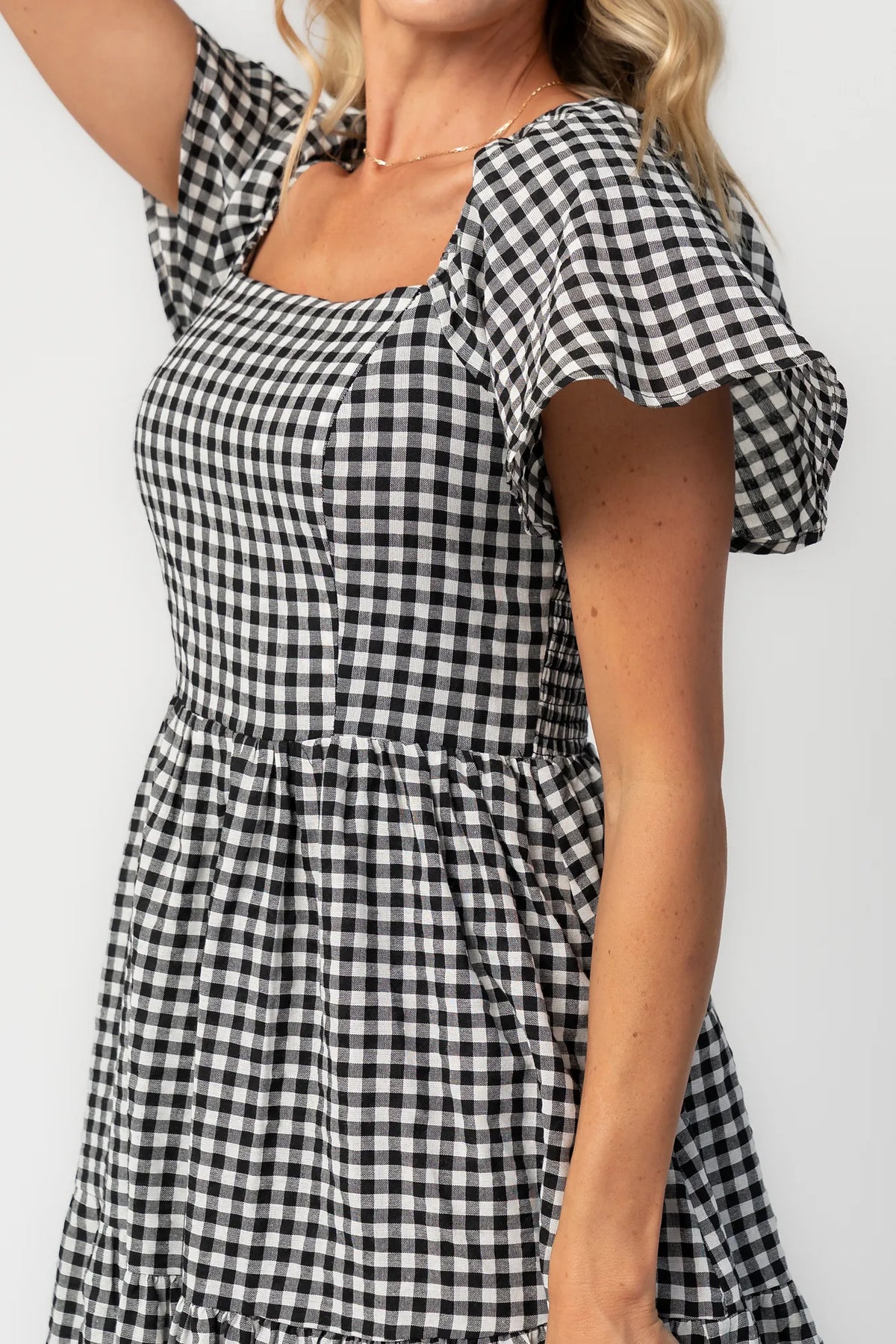 Model wearing a black and white gingham maxi dress with a square neckline, flutter sleeves, and a fitted bodice.