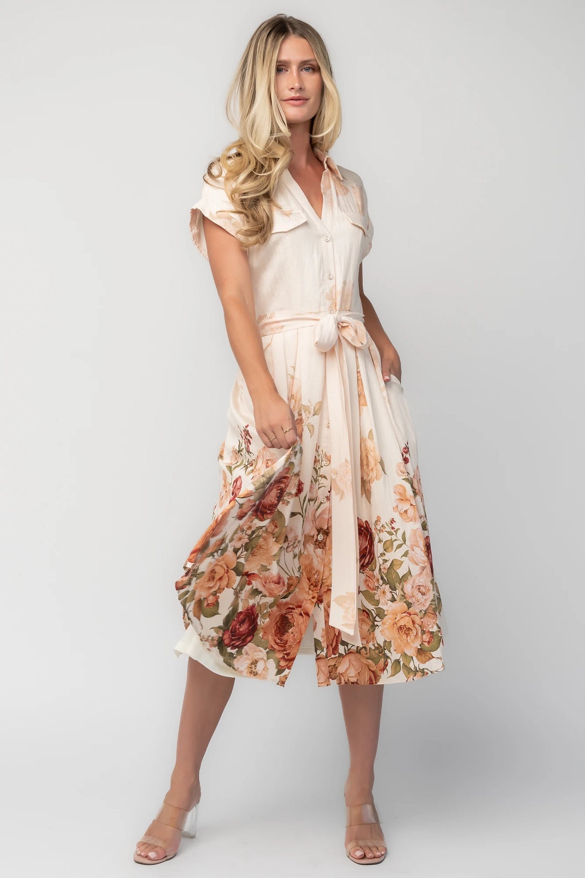 Model wearing a cream floral midi dress with a collared neckline, functional button-front bodice, short sleeves, a removable waist tie, and a flowing midi-length skirt.