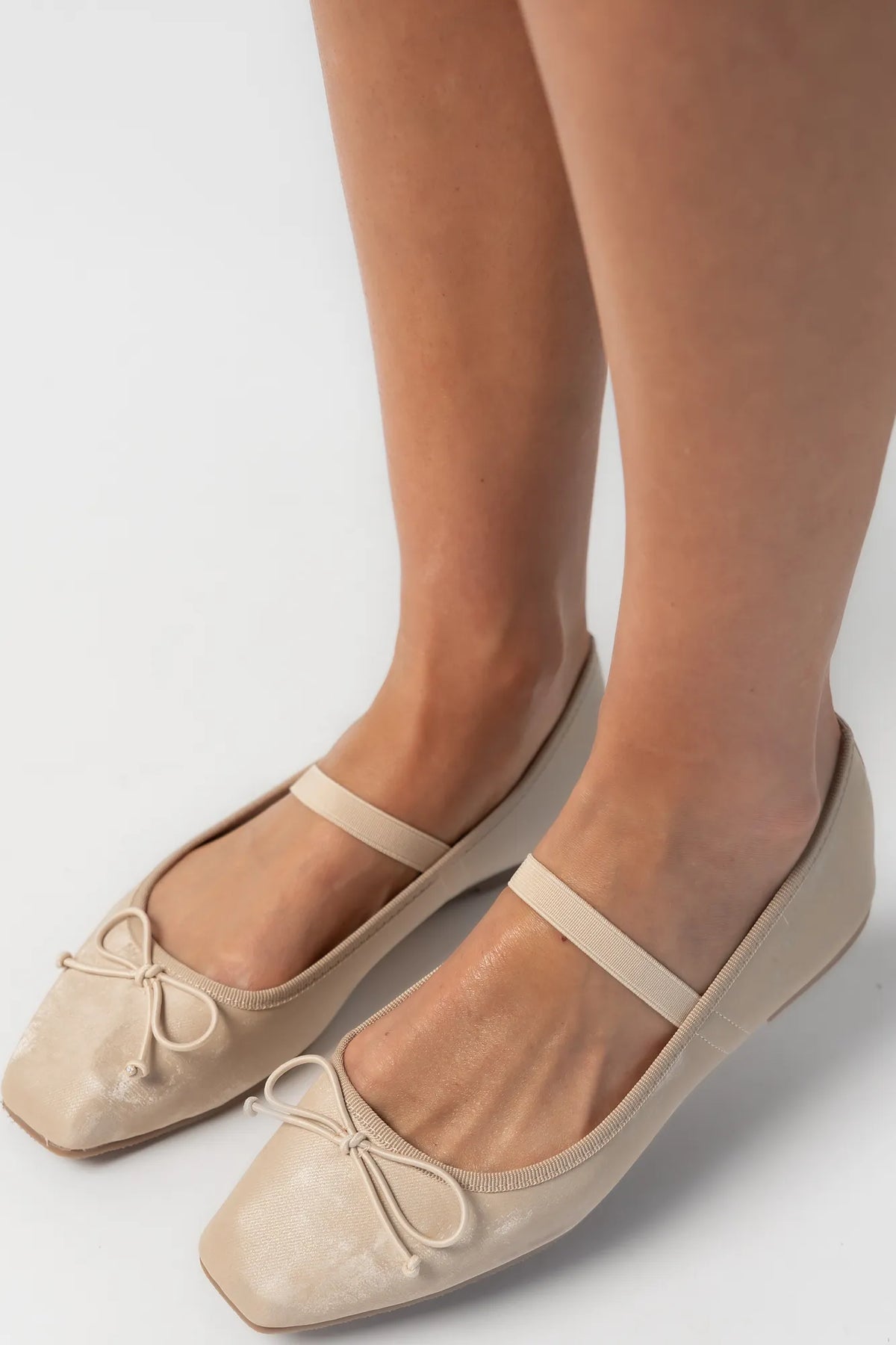 Pair of taupe velvet Mary Jane ballet flats featuring a square toe, delicate bow detail, and elastic strap across the foot. The classic flat silhouette offers a timeless, feminine look for everyday wear.