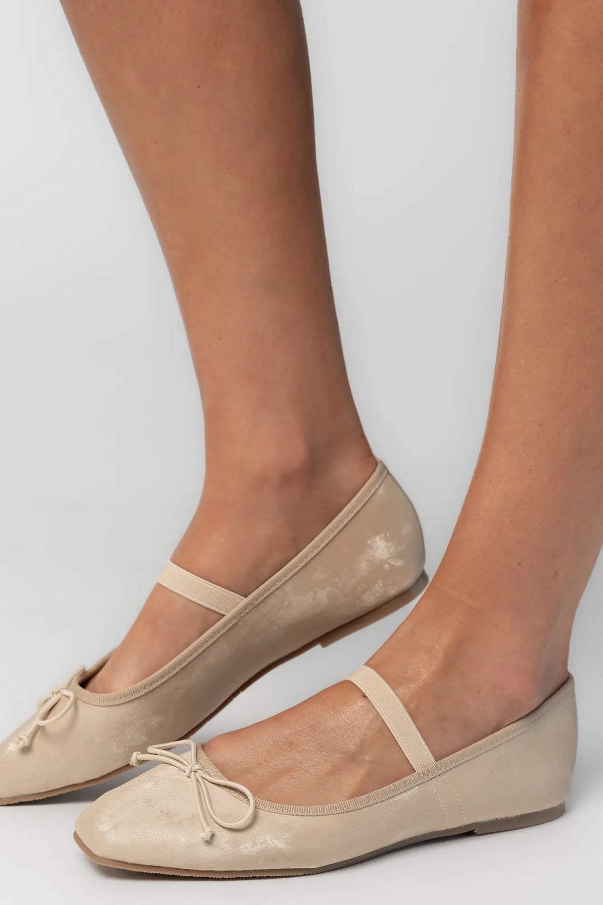 Pair of taupe velvet Mary Jane ballet flats featuring a square toe, delicate bow detail, and elastic strap across the foot. The classic flat silhouette offers a timeless, feminine look for everyday wear.