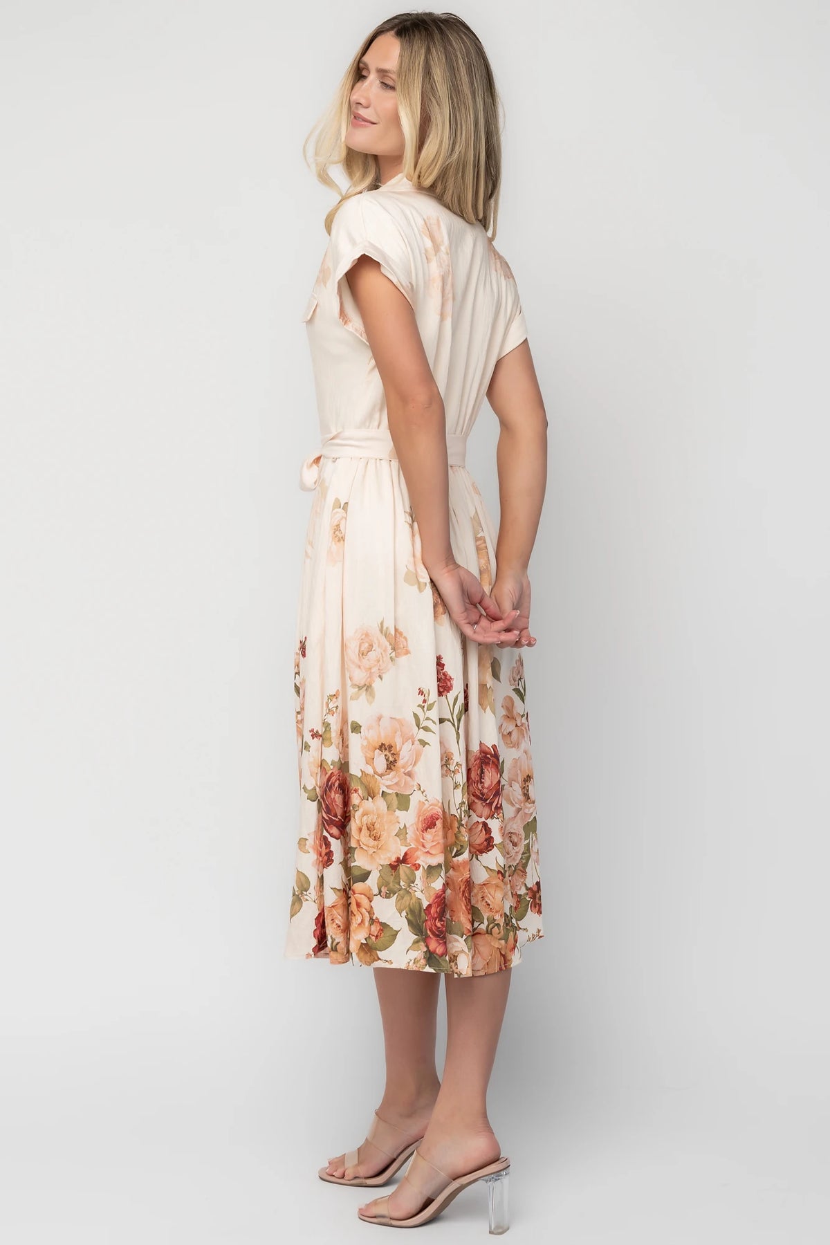Model wearing a cream floral midi dress with a collared neckline, functional button-front bodice, short sleeves, a removable waist tie, and a flowing midi-length skirt.