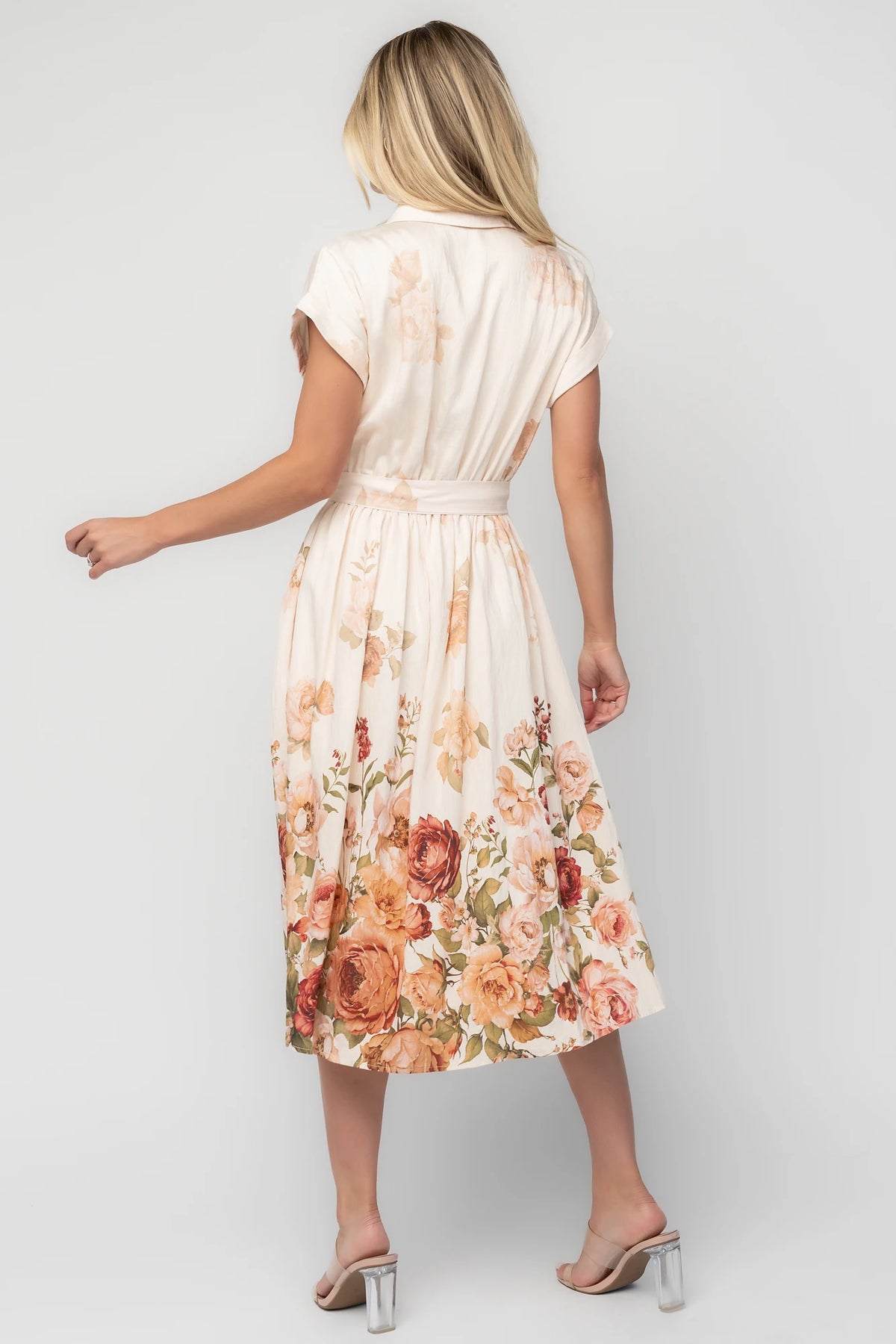 Model wearing a cream floral midi dress with a collared neckline, functional button-front bodice, short sleeves, a removable waist tie, and a flowing midi-length skirt.