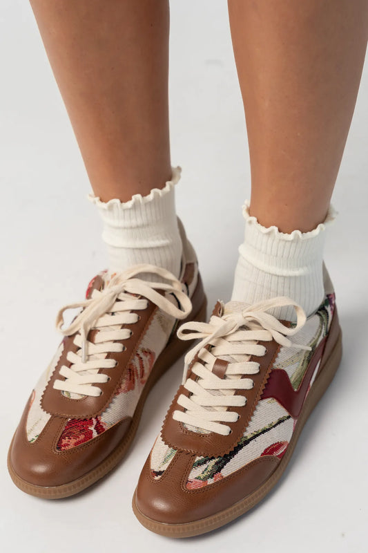 Pair of low-top sneakers  featuring cognac faux leather overlays, floral tapestry panels with rose motifs, and cream laces. The vintage-inspired design combines mixed textures and warm tones for a casual yet elevated everyday look.